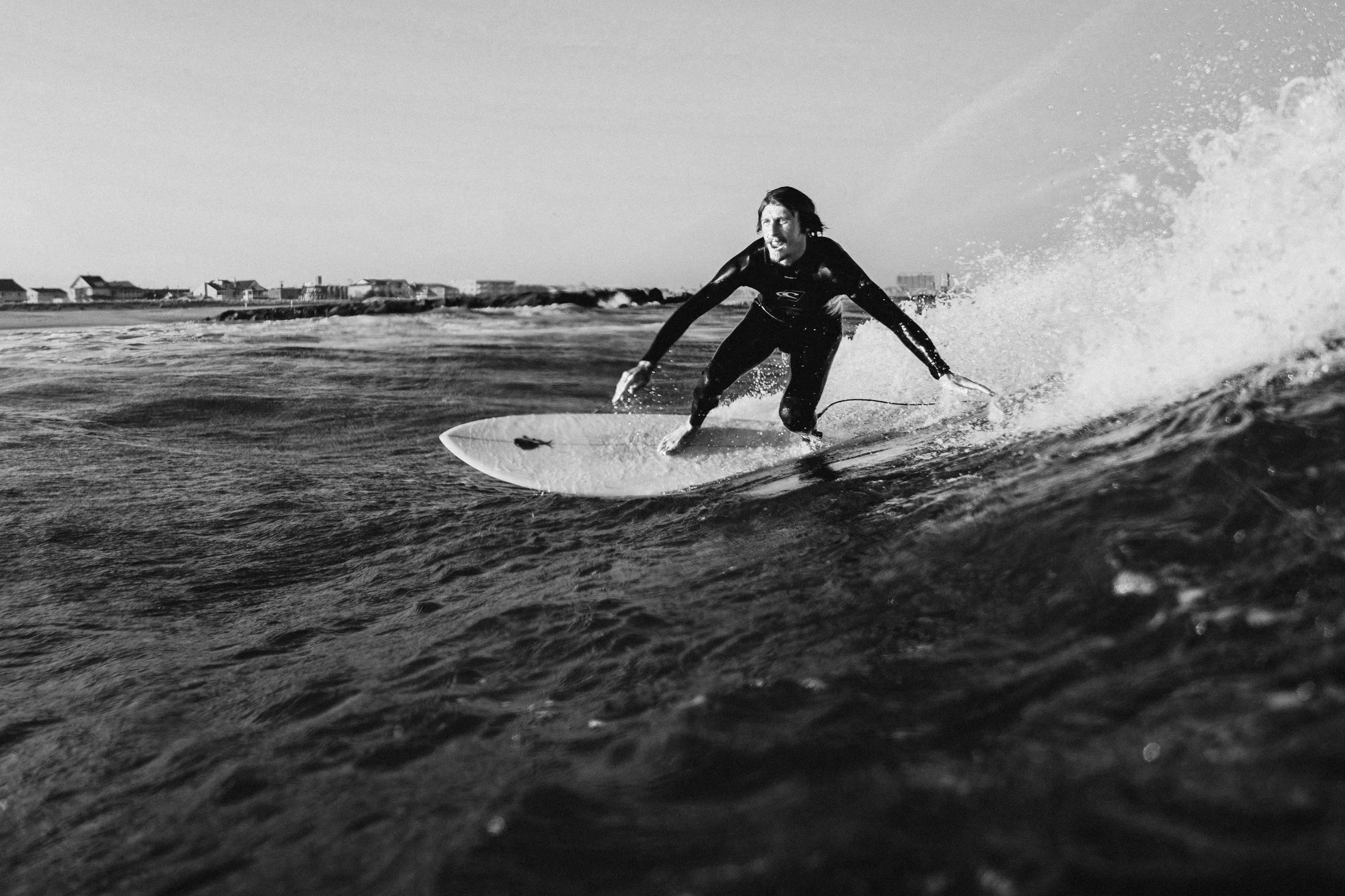 A woman surfing on a wave in the ocean, wearing a wetsuit, with houses in the background.