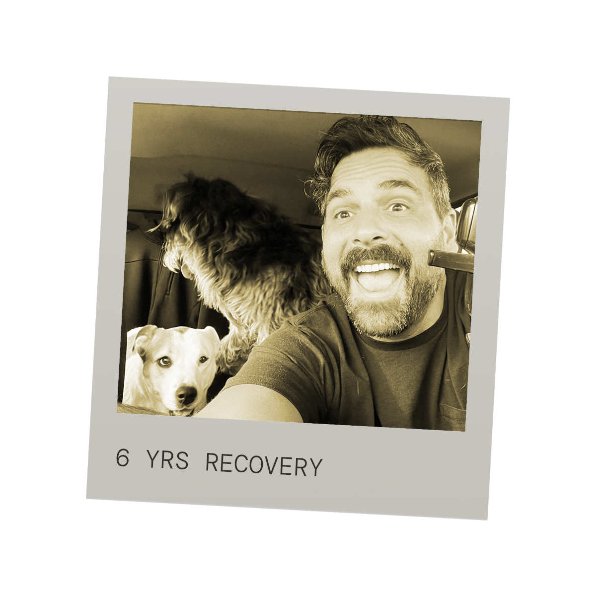 A man taking a selfie with two dogs inside a vehicle. The man is happy, wearing a headset microphone. One dog is light-colored and looking at the camera, the other darker and looking away. The caption reads '6 YRS RECOVERY'.