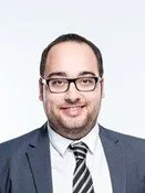 Porträt eines Mannes mit Kurzhaarfrisur, Brille, Anzug und Krawatte, lächelnd.