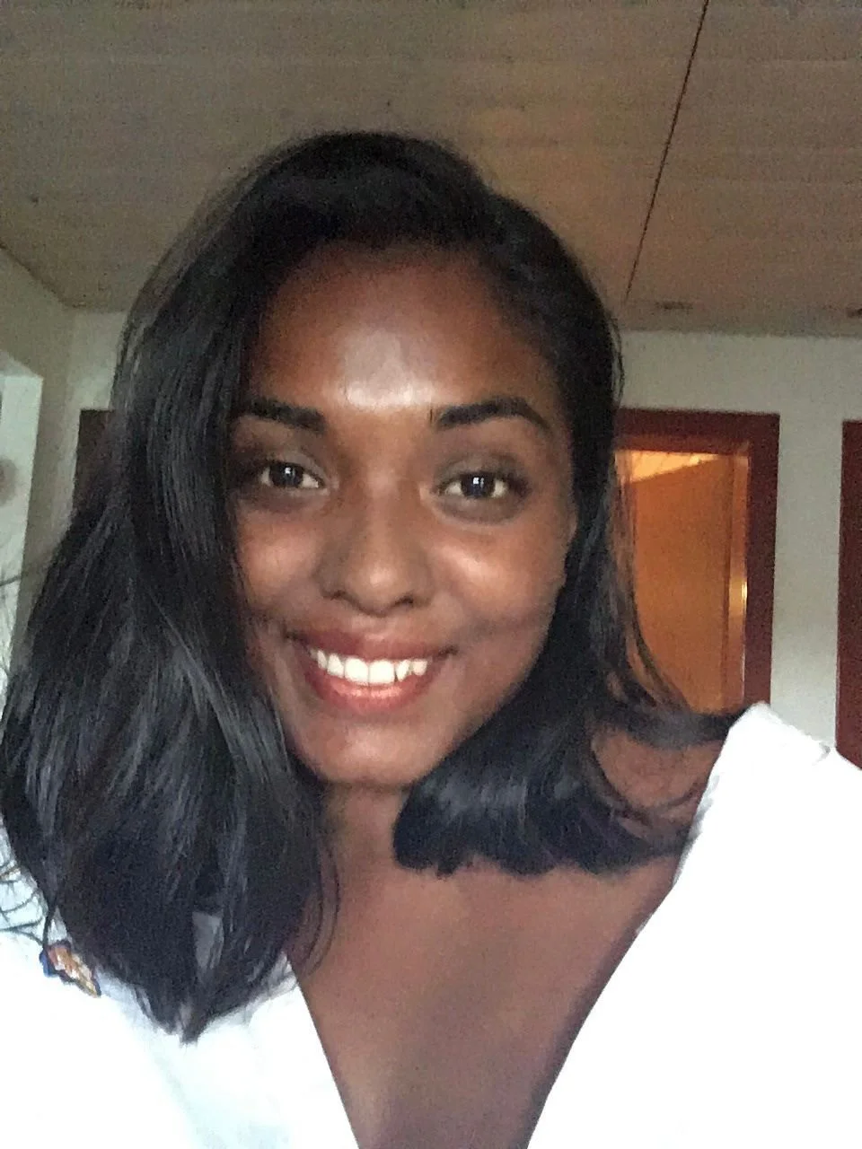 Ein Lächelndes Mädchen mit schwarzem Haar und brauner Haut, das ein weißes Oberteil trägt.