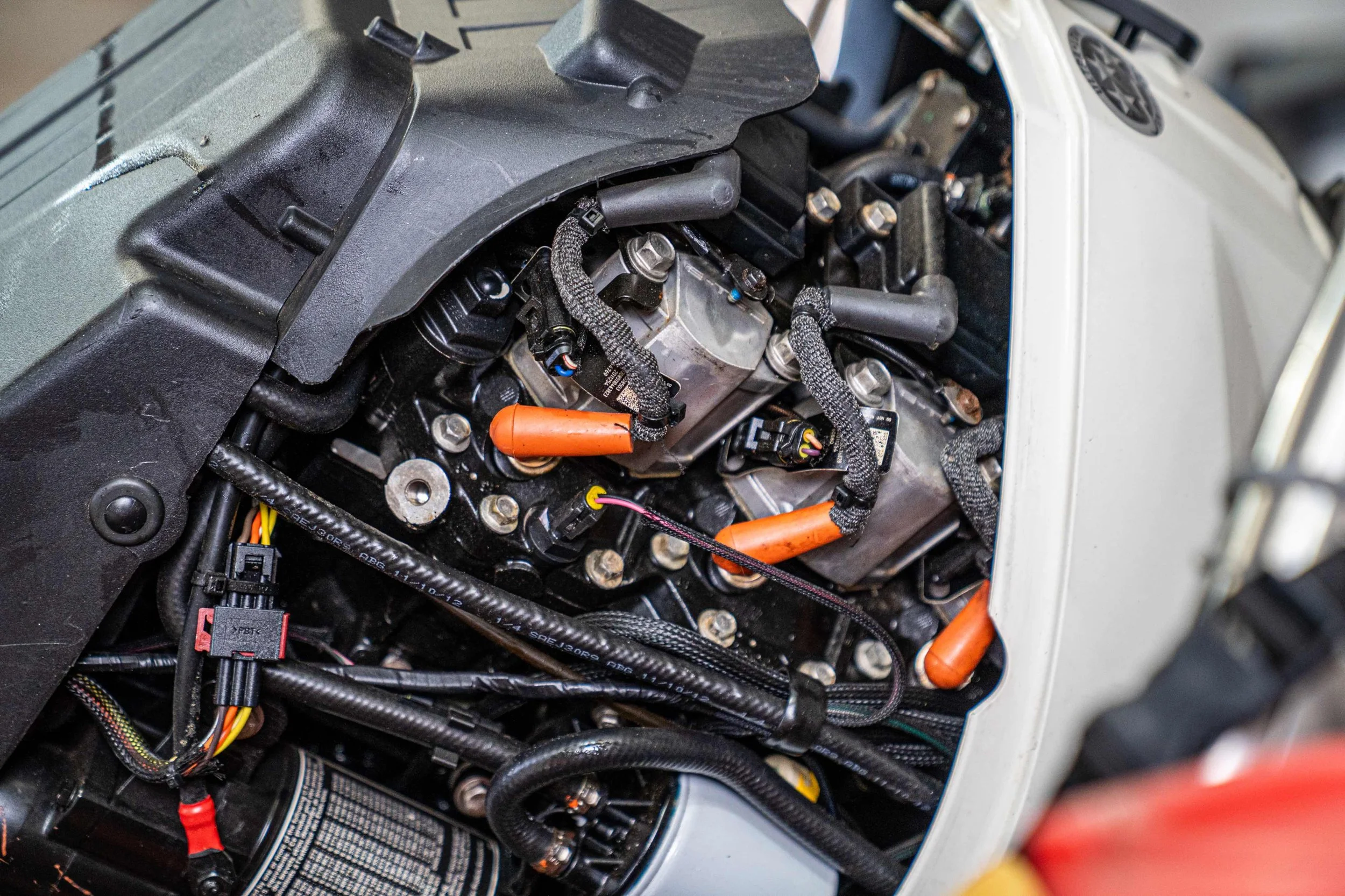 Close-up of a motorcycle engine with visible wiring and components, partially covered by a black plastic cover.