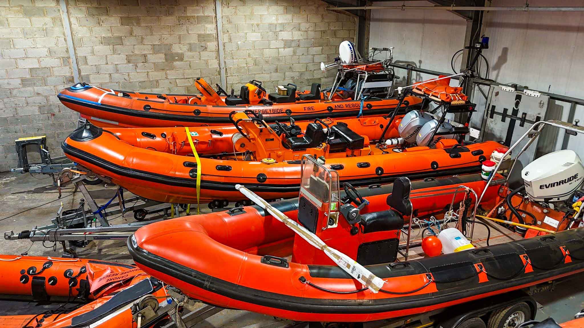 Group of orange rescue boats inside a storage warehouse, equipped with motors, seats, and safety gear.