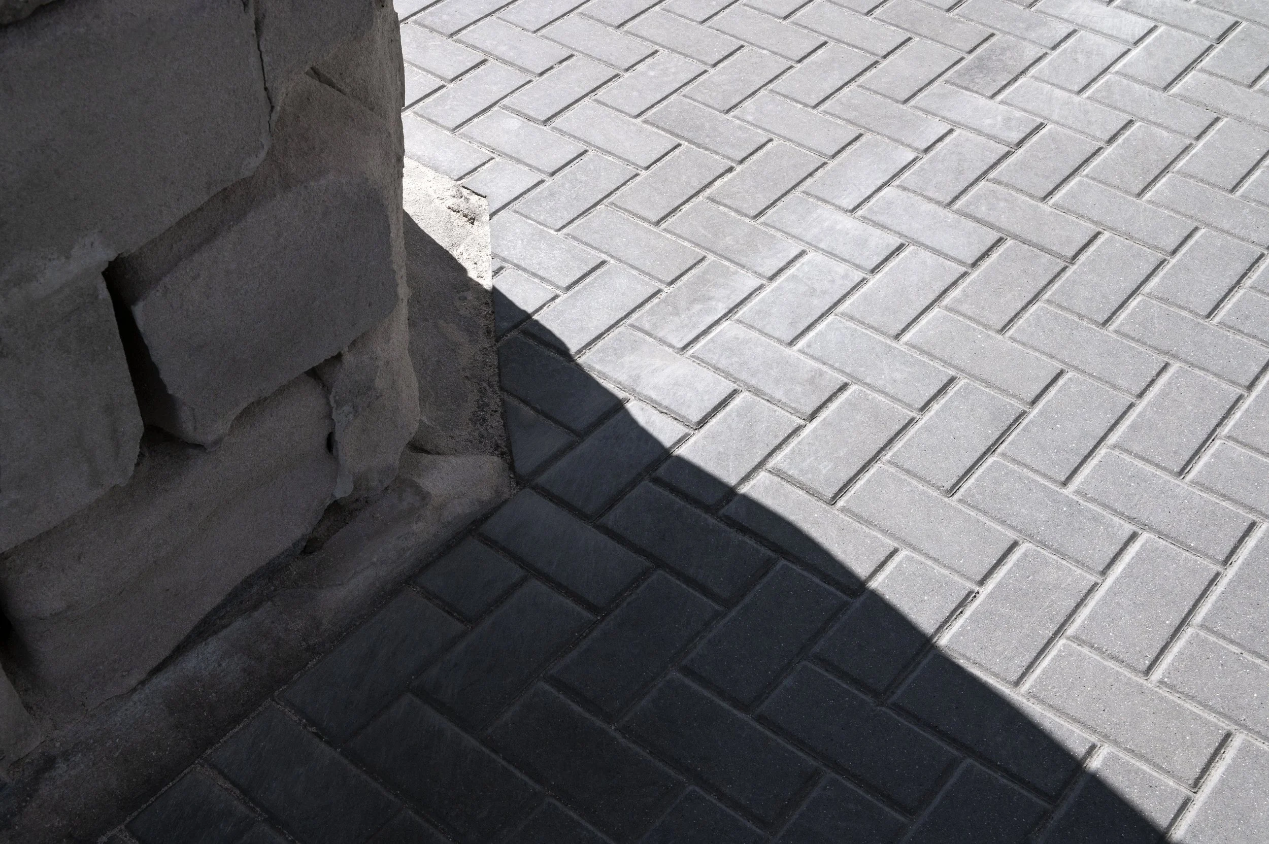 Close-up of a corner where a brick wall meets a brick sidewalk, highlighting the shadow cast at the intersection.