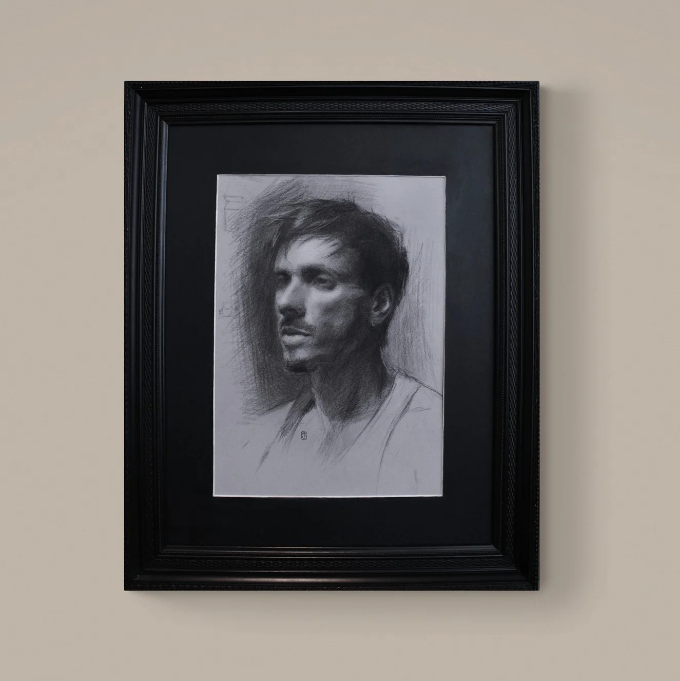 Framed pencil sketch portrait of a young man with messy hair on a beige wall.