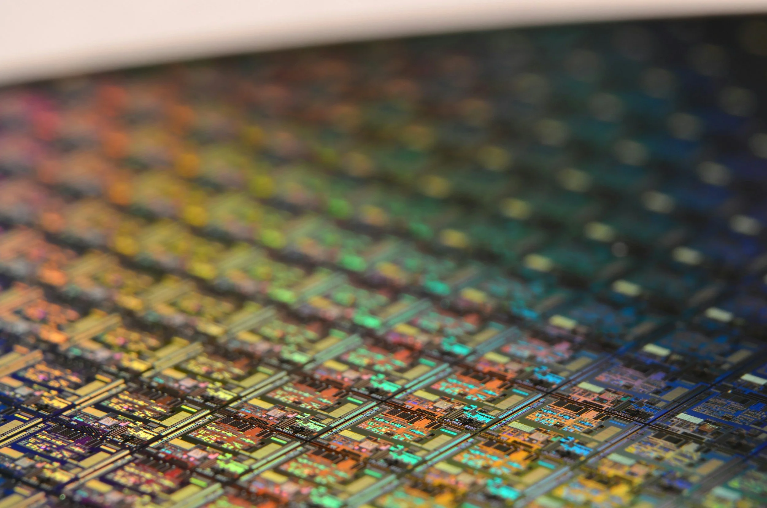Macro close-up of a colorful iridescent silicon semiconductor wafer with intricate circuit patterns, representing AI technology and the workforce changes it is driving in the tech industry.