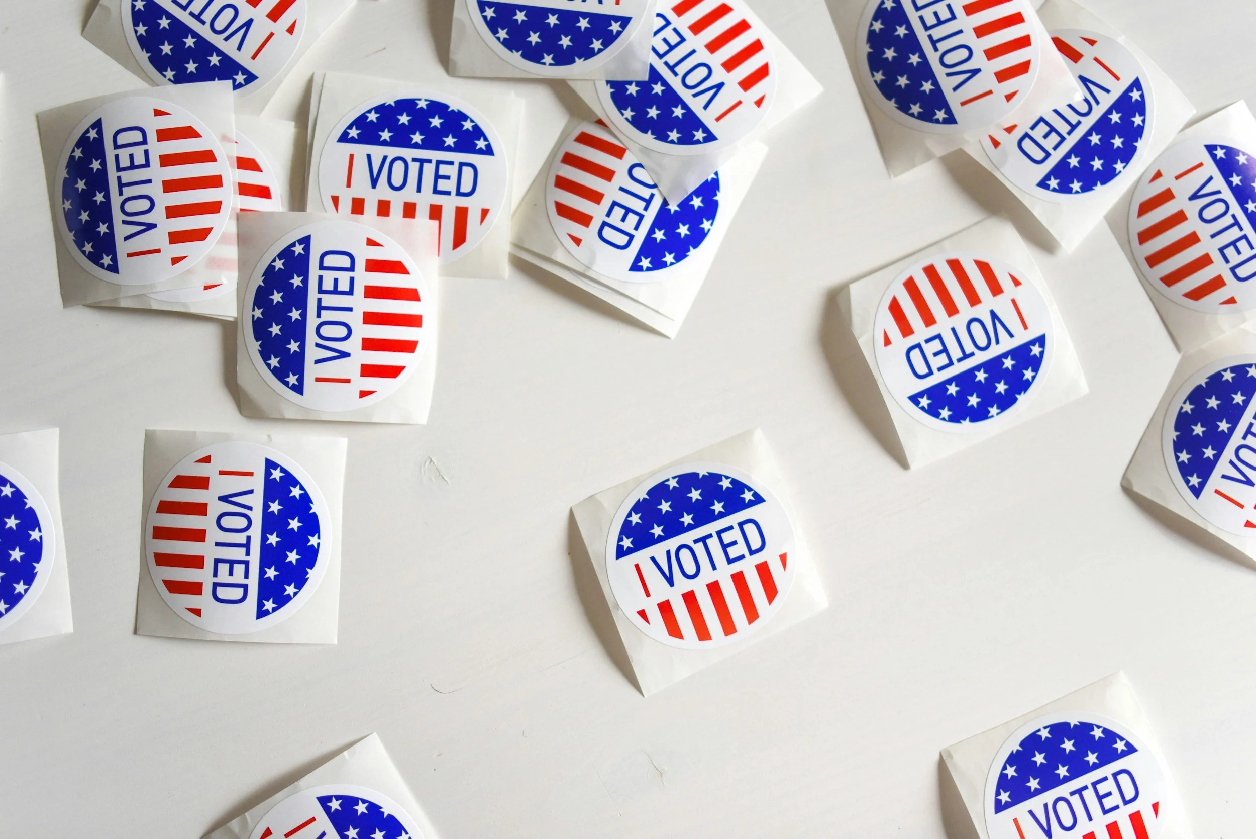 Scattered red, white, and blue "I Voted" stickers on white surface, representing the 2024 presidential election that brought the return of Schedule F as Schedule P/C.