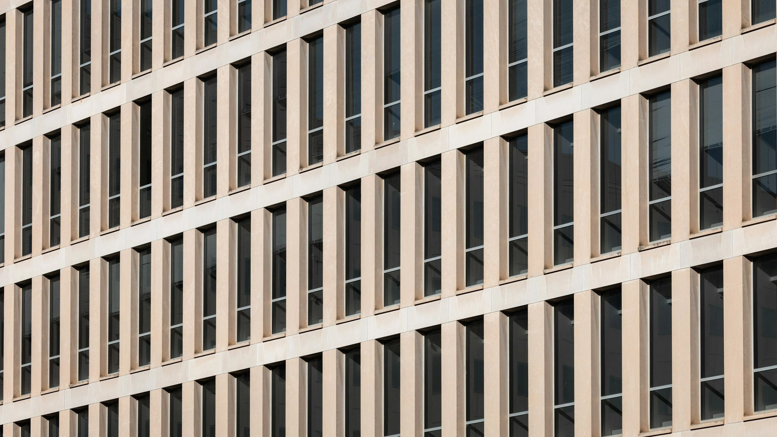 Close-up of a repetitive grid of windows on a beige government-style office building facade, evoking the federal bureaucracy behind Schedule P/C implementation for the federal workforce.