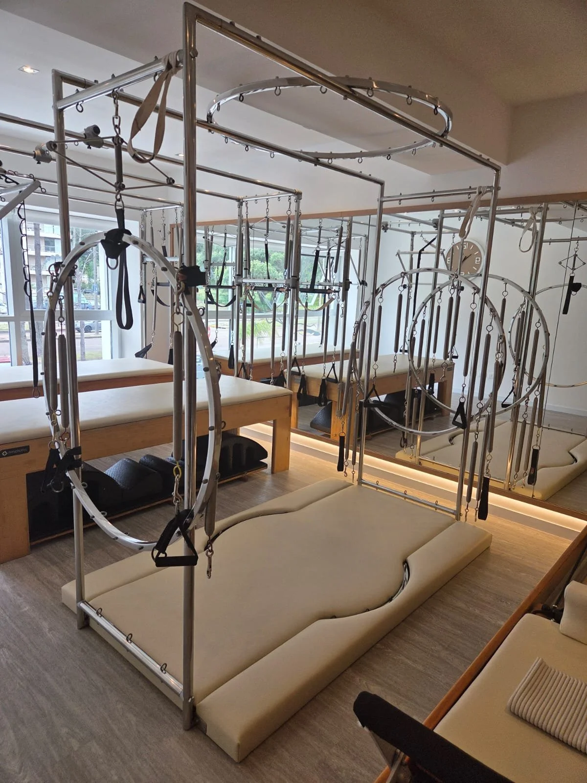 Indoor Pilates studio with metal exercise equipment, windows, and padded floor mats.