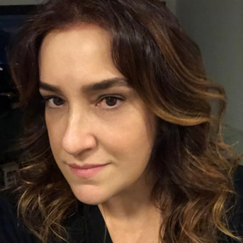 Close-up of a woman with wavy brown hair and light makeup, looking at the camera with a slight smile.