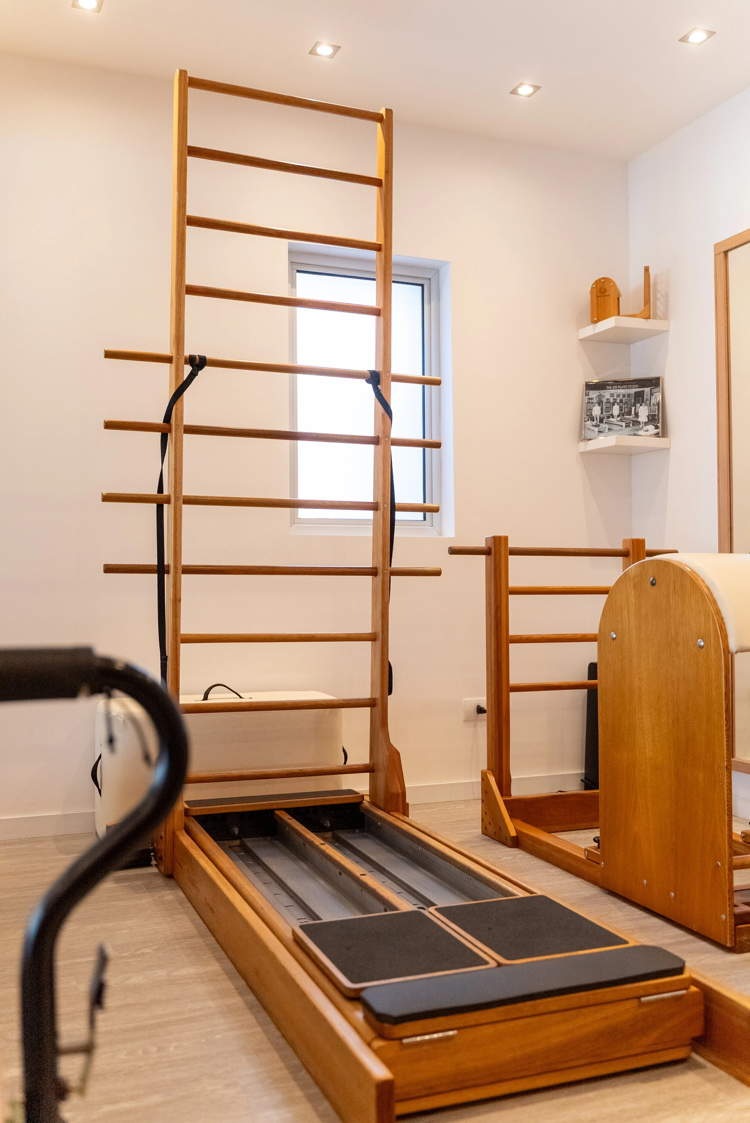 Pilates reformer machine and workout equipment in a modern fitness studio with wooden accents and large window.