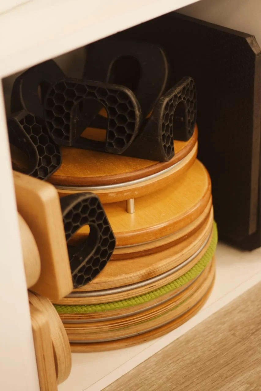 Stack of wooden and bamboo cutting boards with black plastic rubber grips on top, inside a cabinet or shelf.