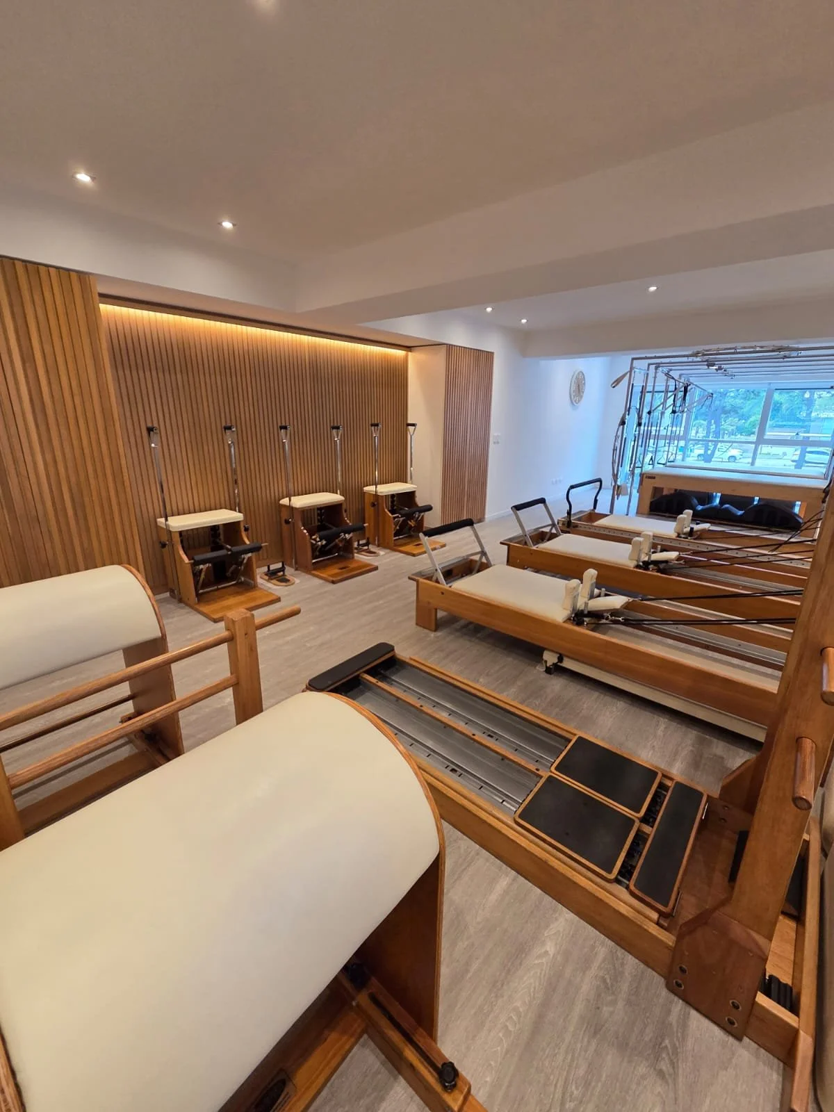 Pilates reformer machine and workout equipment in a modern fitness studio with wooden accents and large window.