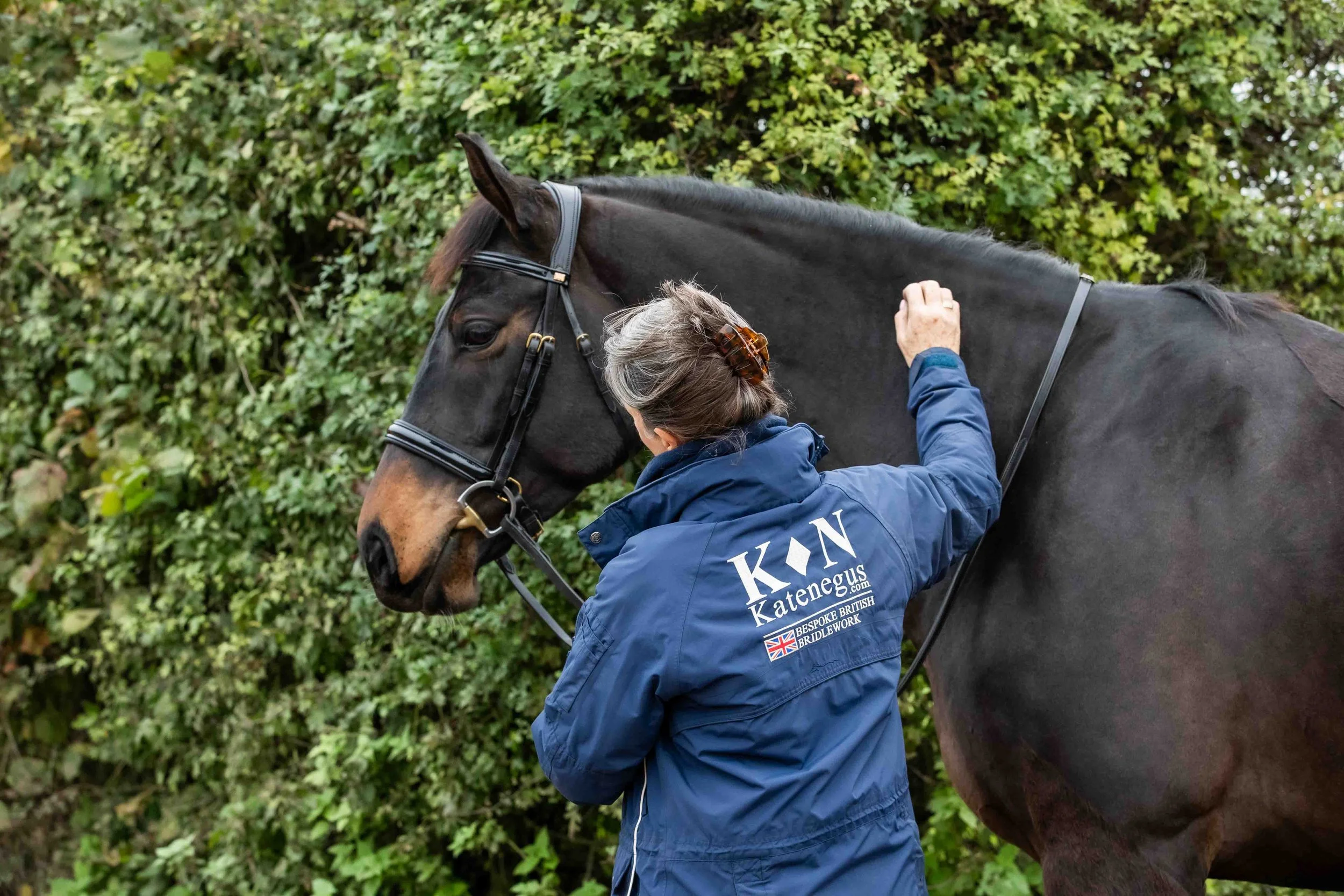 Owner of Kate Negus grooming a black horse wearing a premium Kate Negus Bridle.