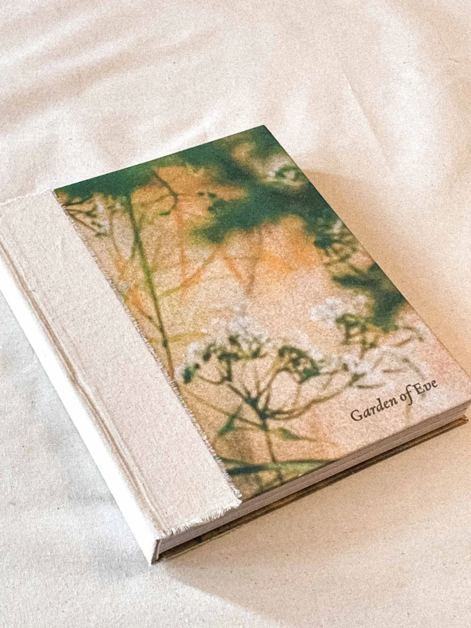 Close-up of a book with a watercolor illustration of leaves and branches on the page, partially open, titled 'Garden of Eve'.
