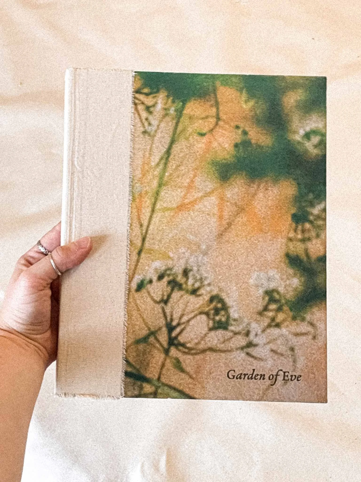 A hand holding a fabric sample with printed plant and floral designs, and the text 'Garden of Eve' on it.