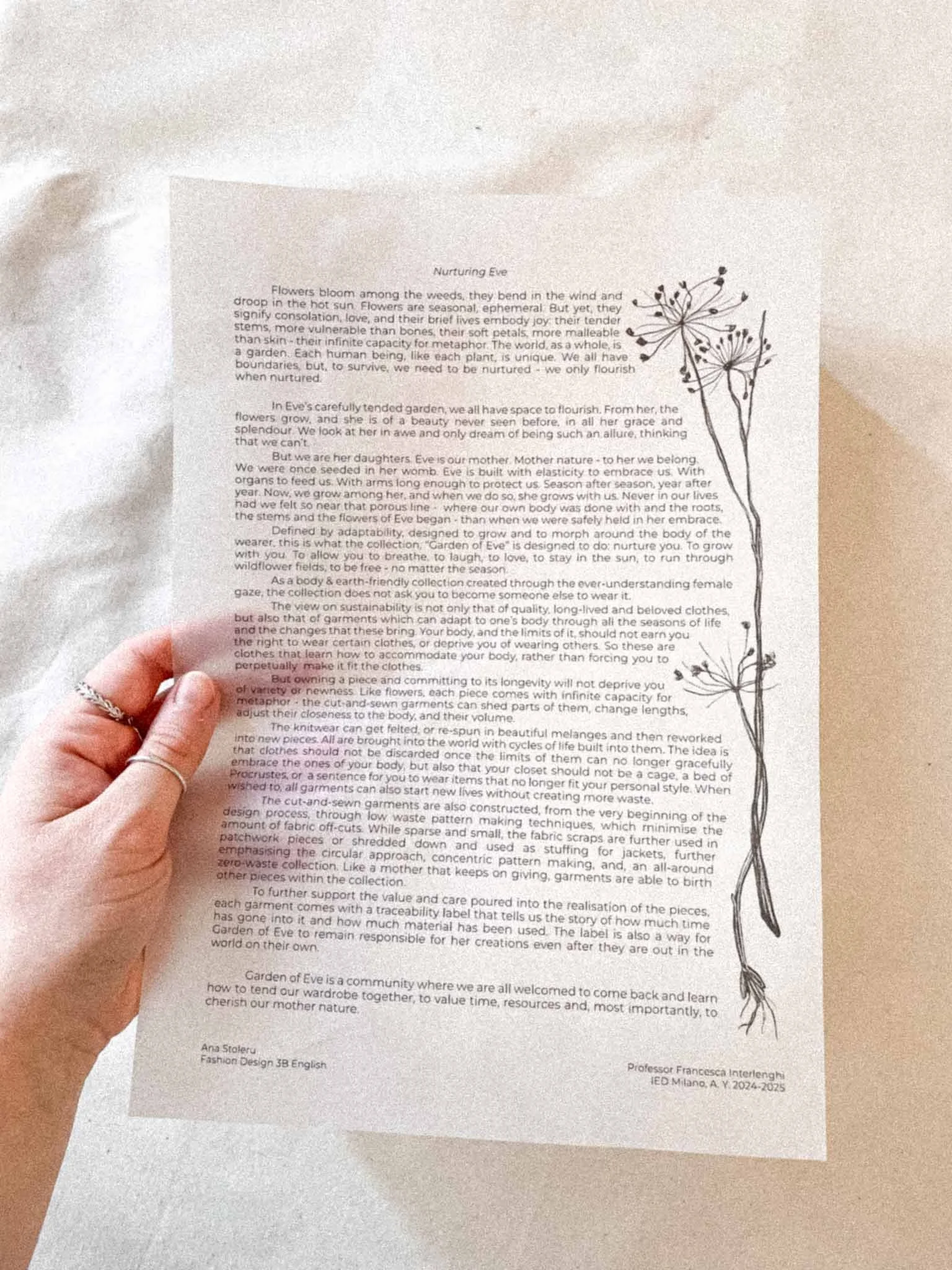 A person holding a sheet of paper with printed text, featuring a black botanical line drawing of a flowering plant on the right side.