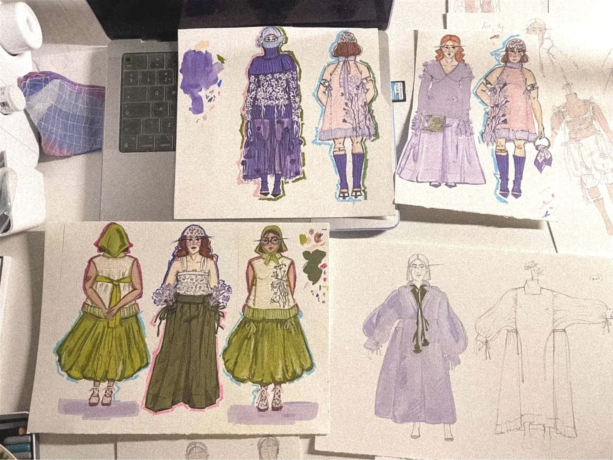 Colorful fashion sketches of women in various dresses, displayed on a desk with art supplies around.
