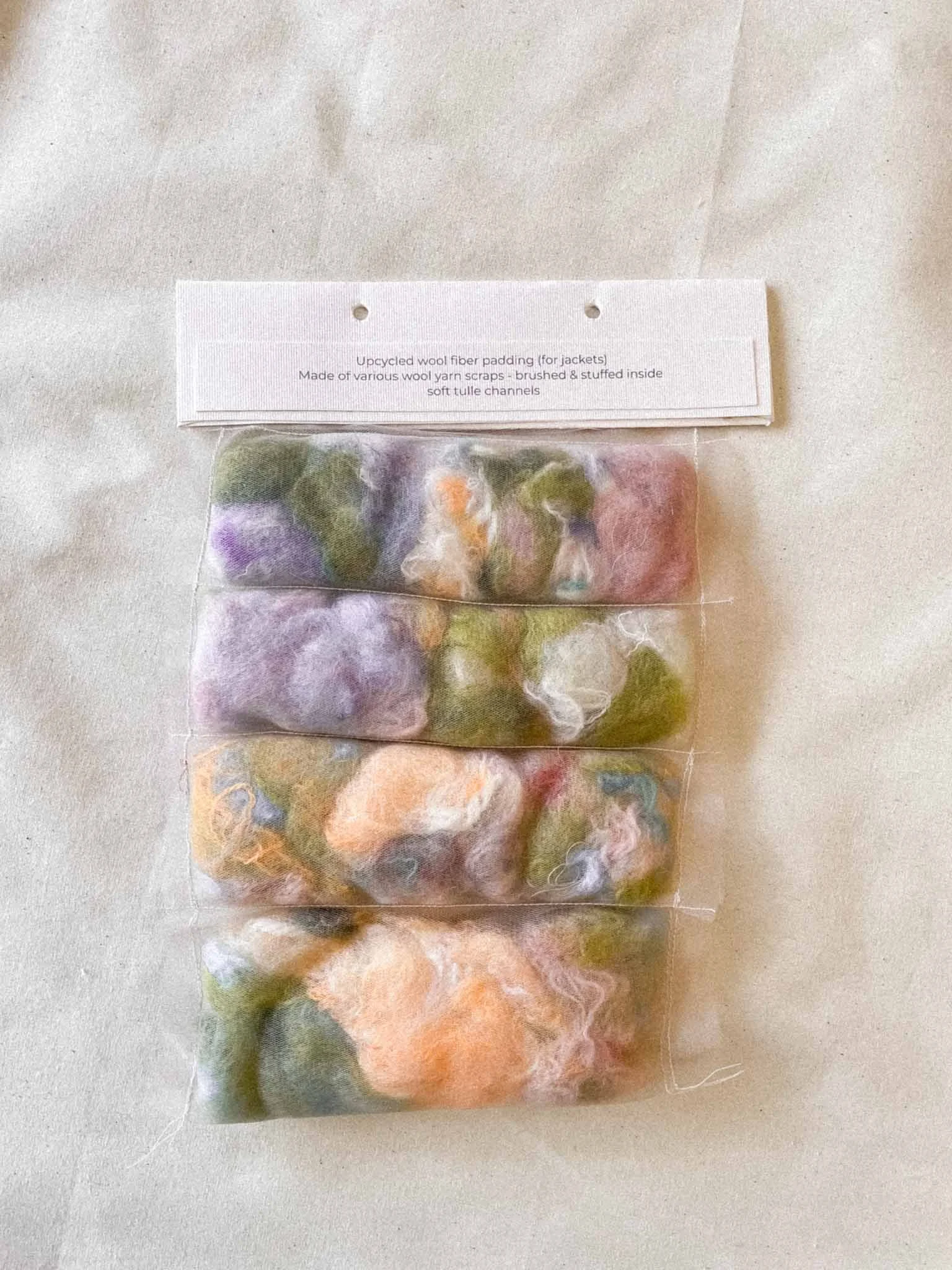 A clear plastic bag filled with felted wool yarn scraps in various colors, labeled as upcycled wool fiber padding for jackets.