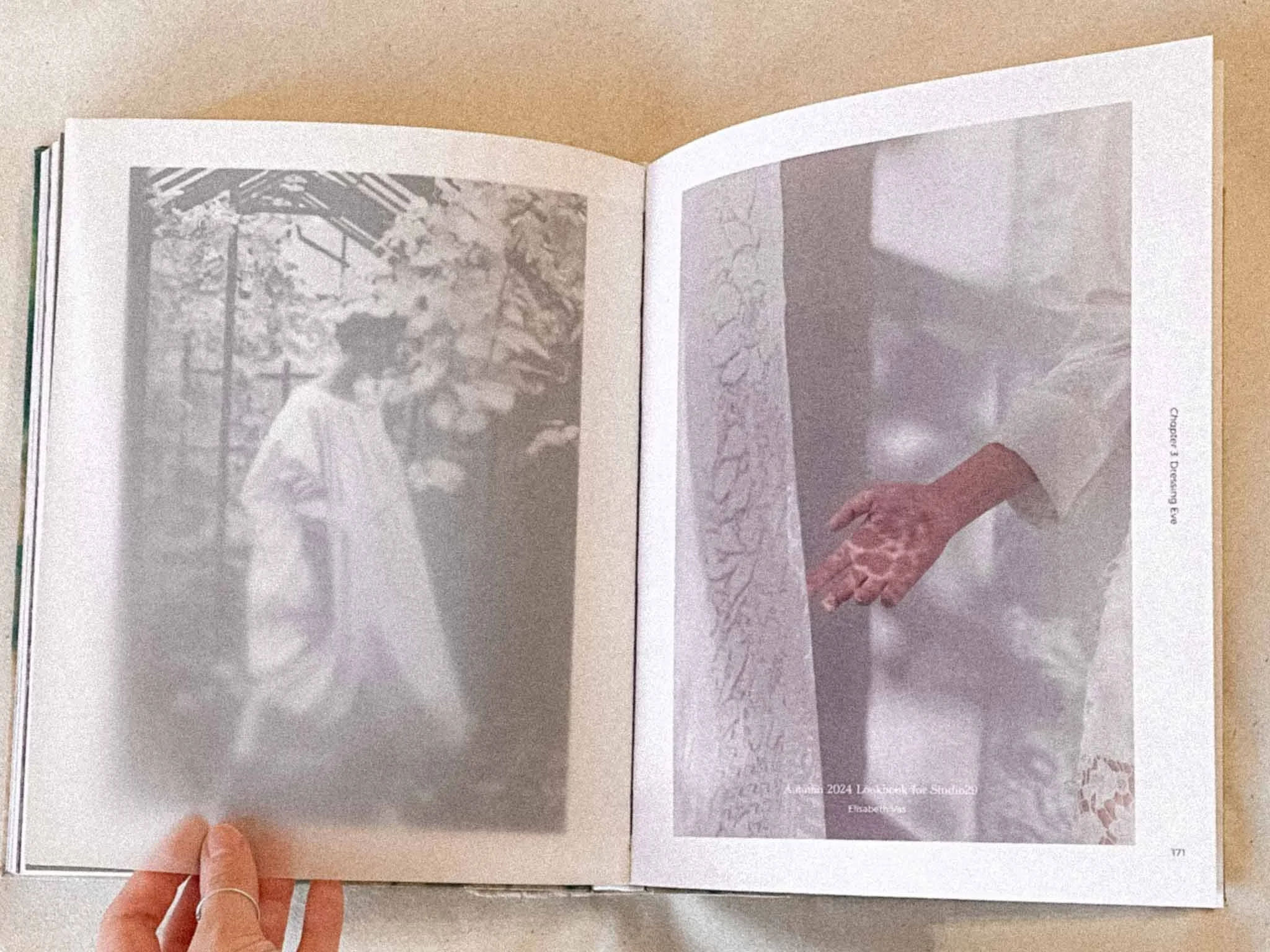 Open book showing black and white images and text on pages, held by a person with a thumb and index finger.