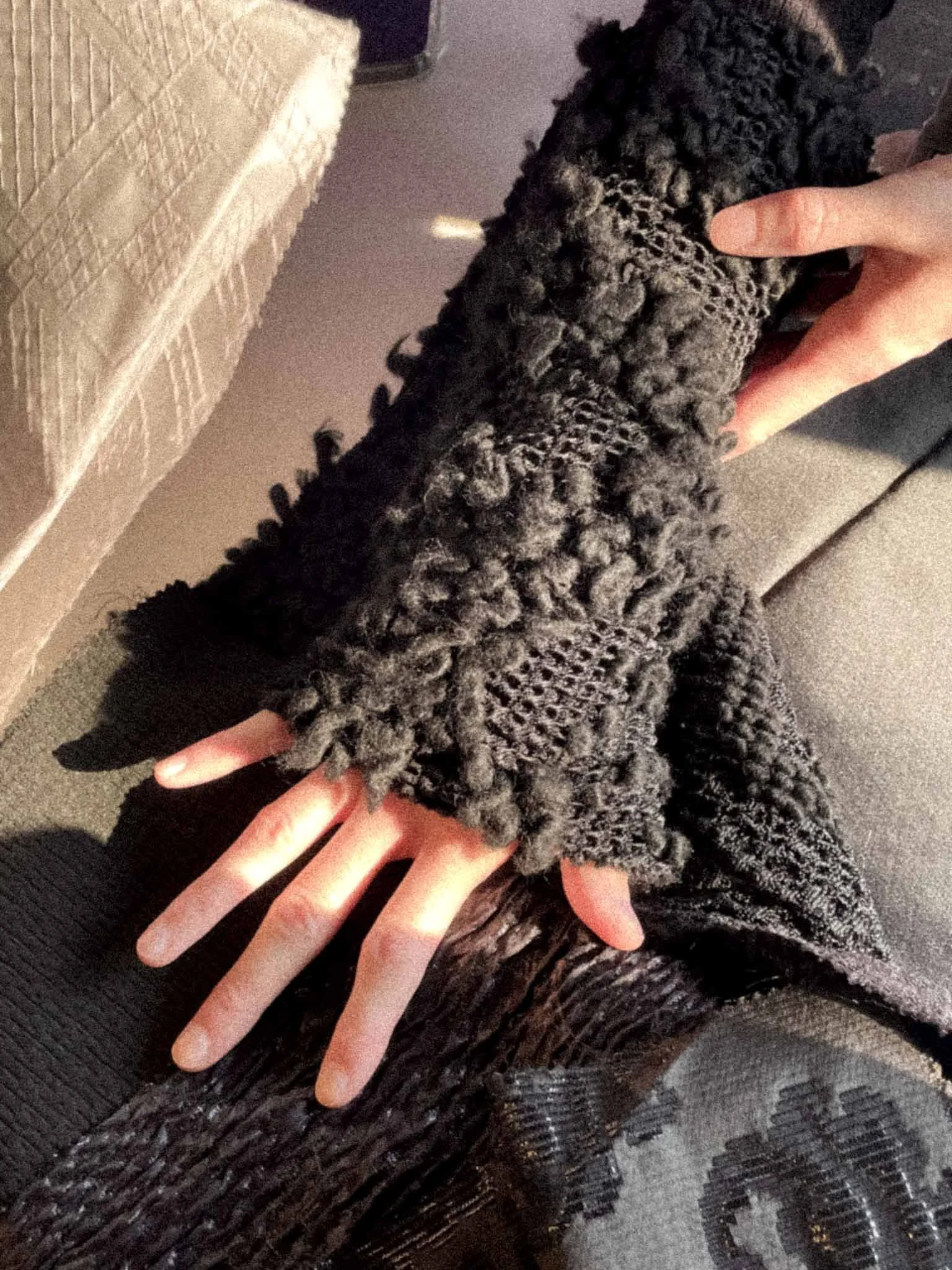 A person holding a black and gray fluffy dog on a black textured surface. The person's fingers are visible supporting the dog.