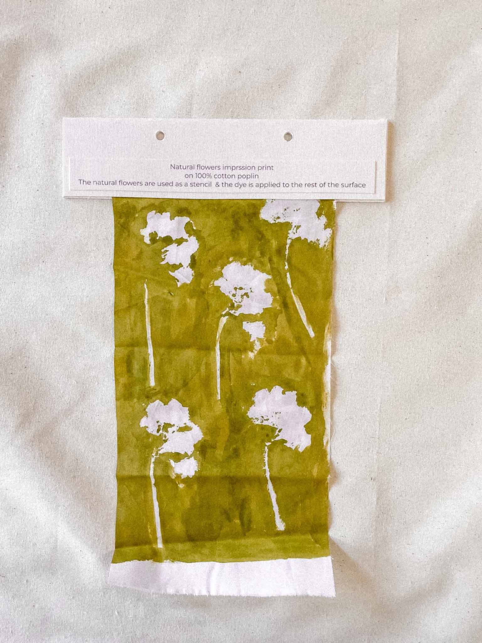 A sheet of yellow-green tissue paper with white floral silhouettes printed or painted on it, placed against a white background, with a card above it labeled with details about the print process.