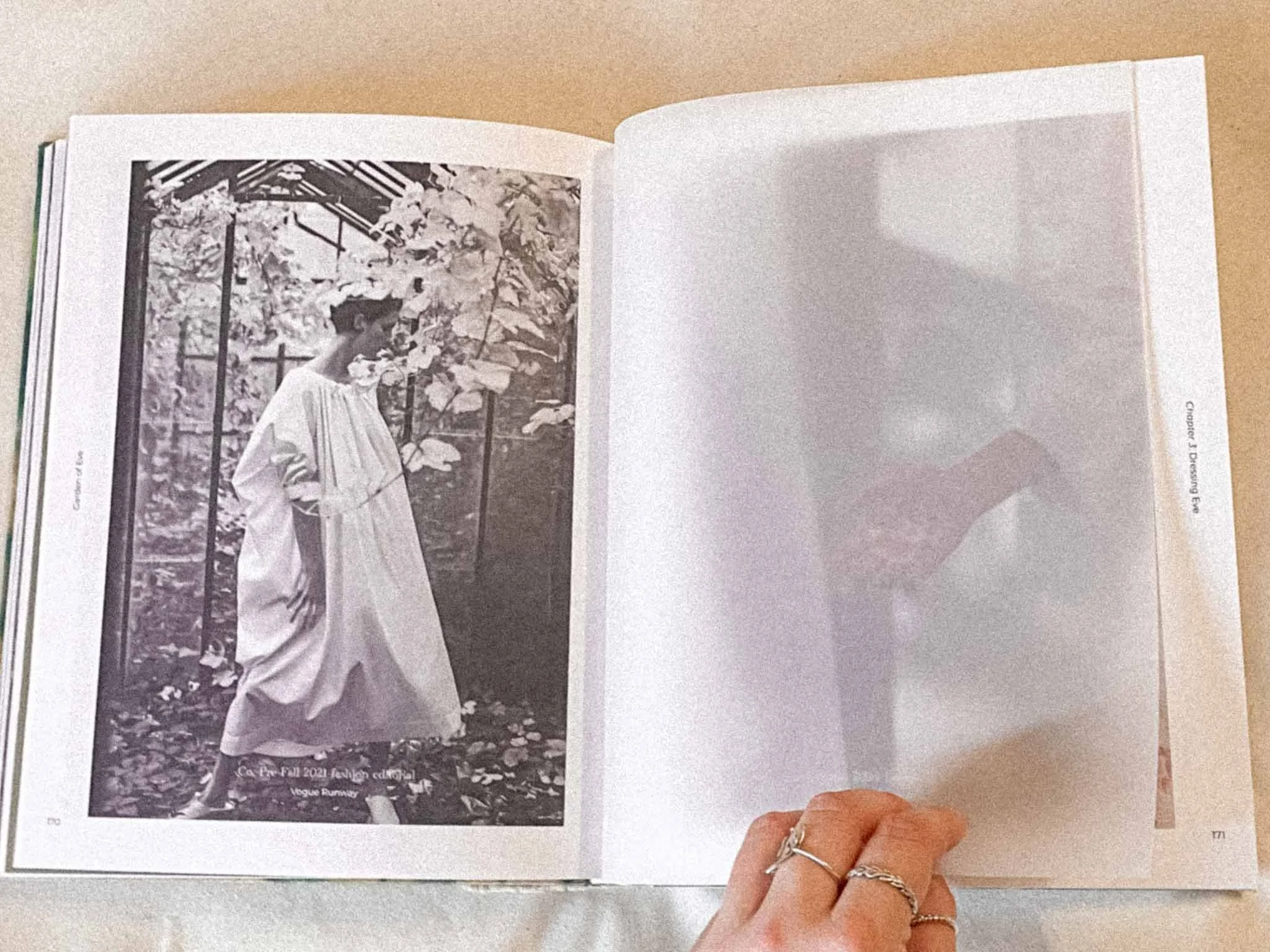A person holding a book open to a black and white photograph of a woman in a wedding dress outdoors, with trees and leaves in the background.