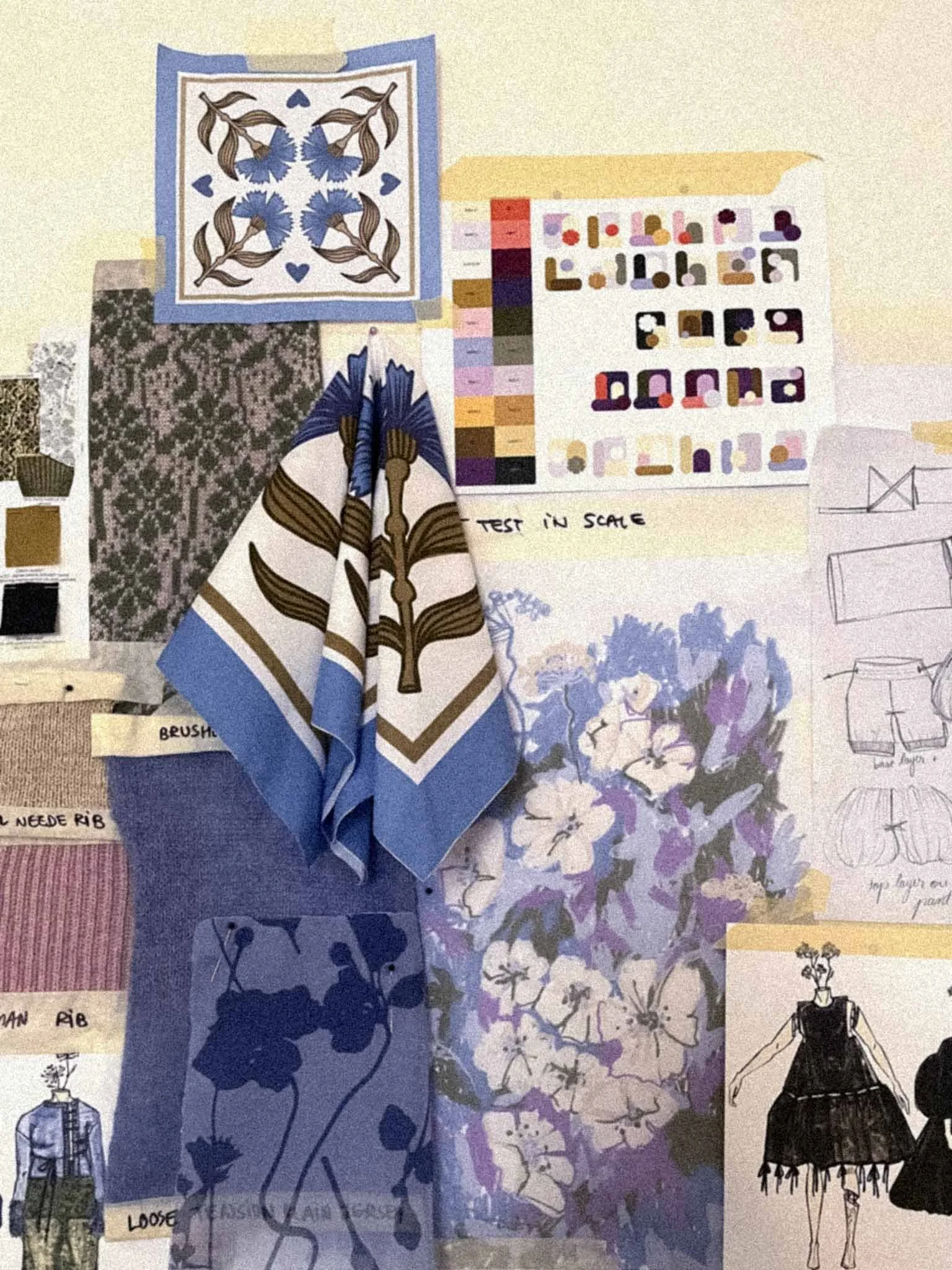 A display of fabric samples and design sketches for fashion and textile projects, including a large floral and leaf print fabric, color swatches, and a sketch of a woman in a dress.