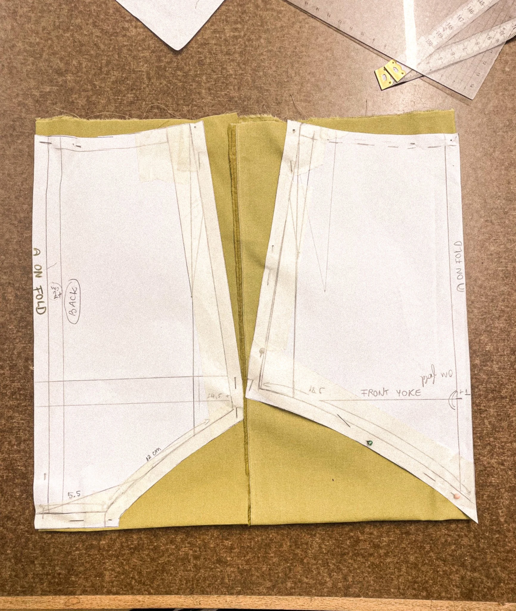Pattern paper pieces, rulers, and template outlines for a sewing project laid out on a brown work surface.