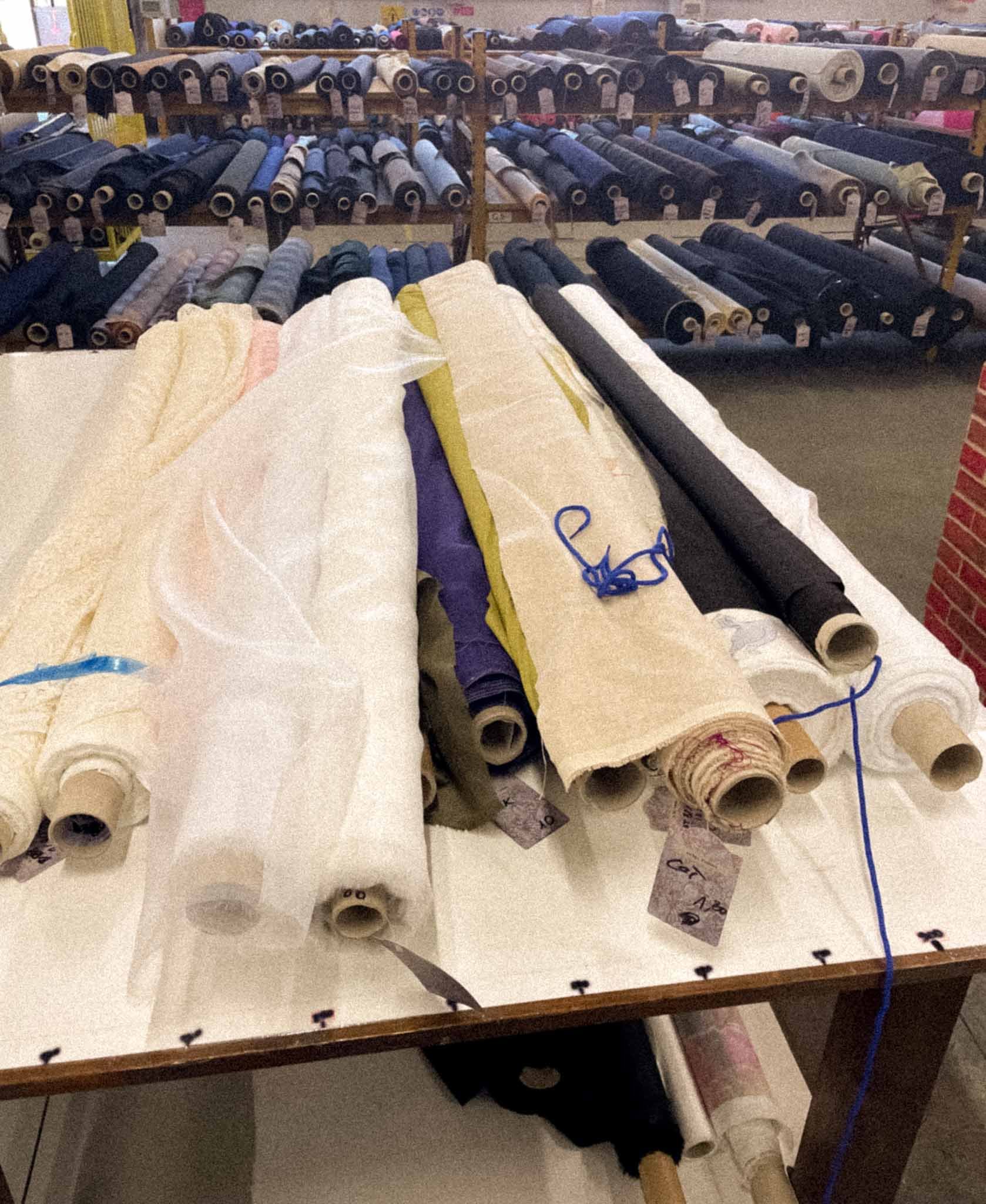 Various rolls of fabric in different colors and textures stacked on shelves and lying on a table.