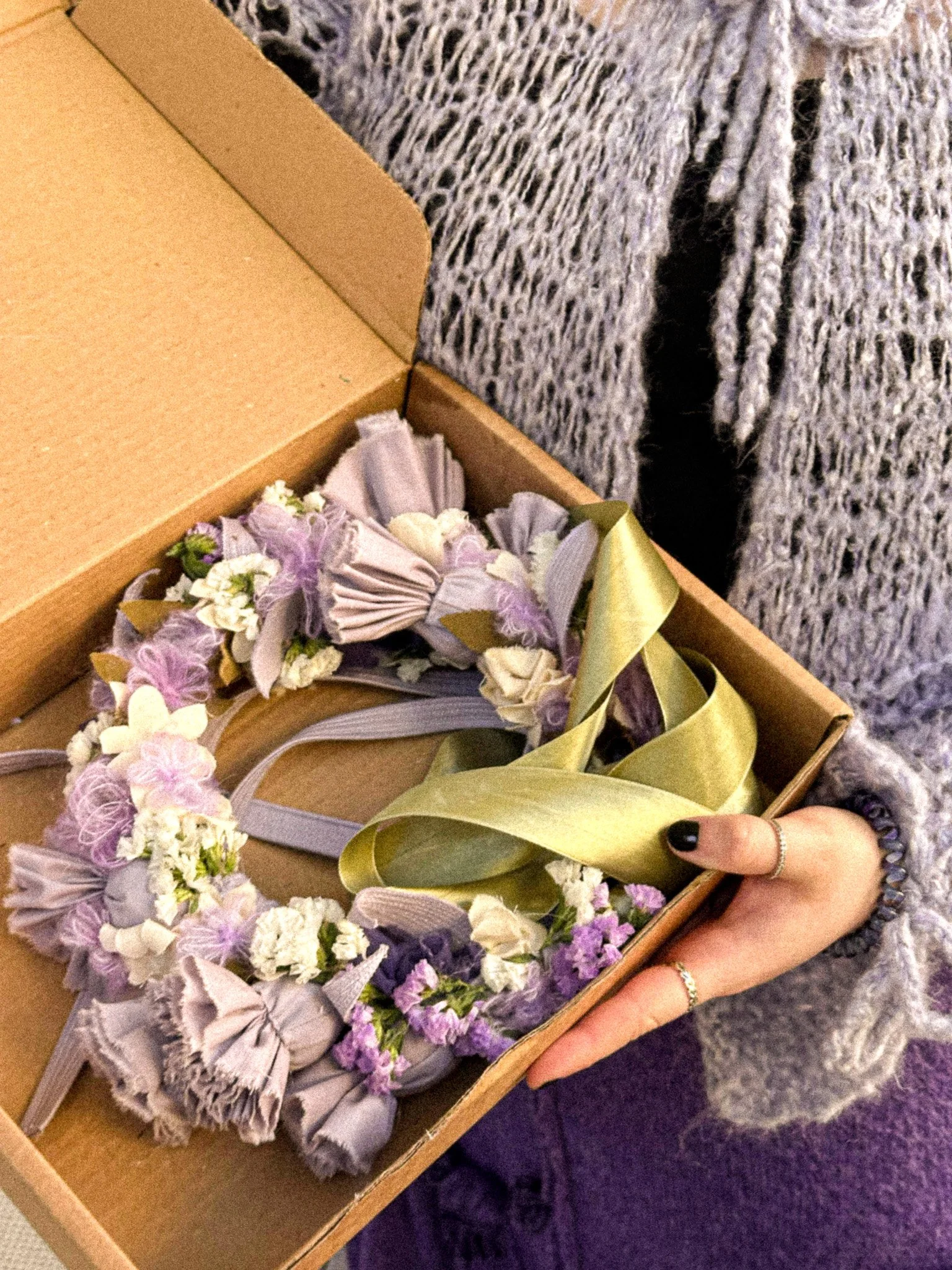 A person holding a wedding bouquet in a cardboard box, with a gray and white patterned sweater visible.