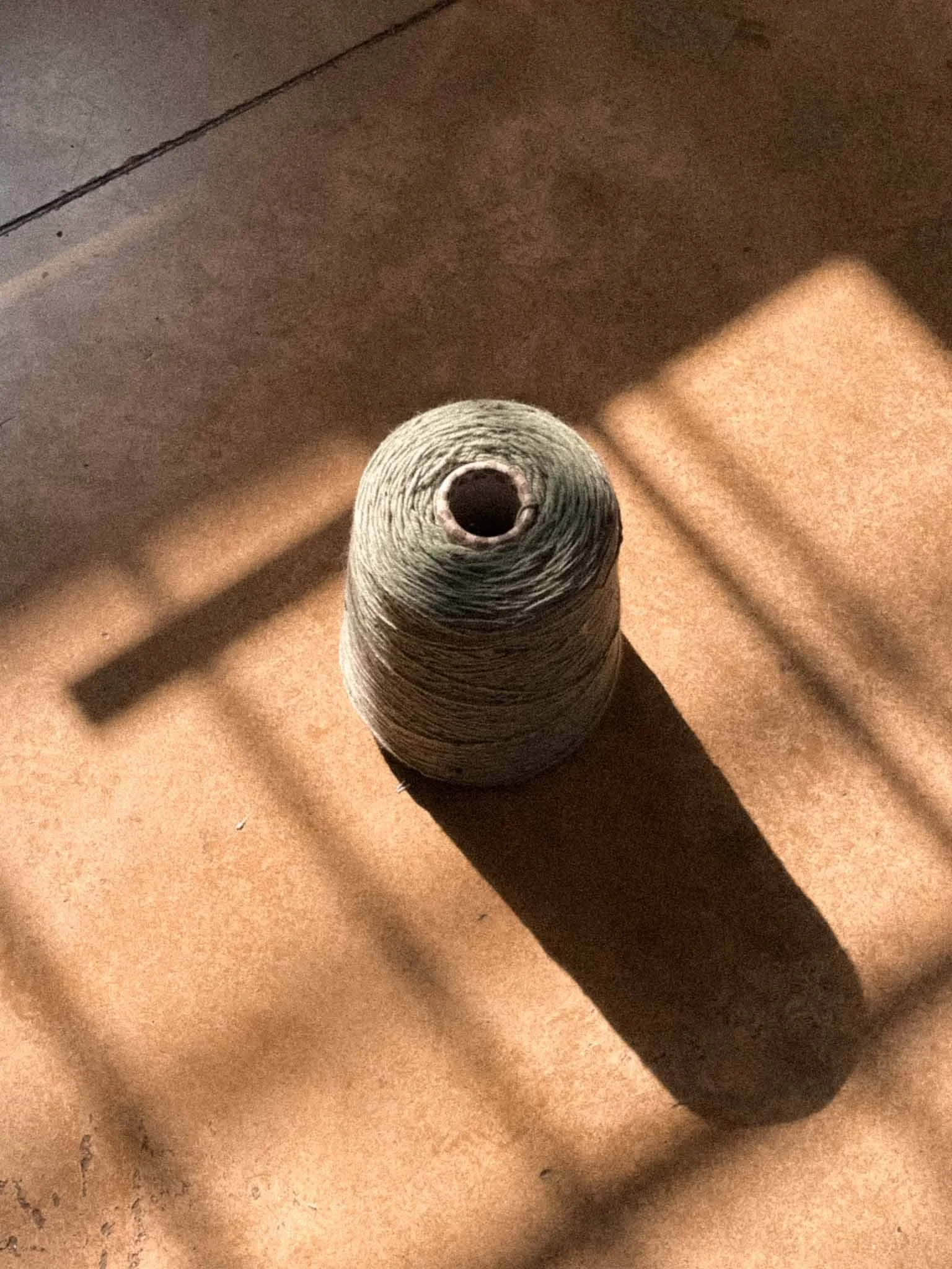 A spool of gray thread placed on a beige surface, casting a shadow.