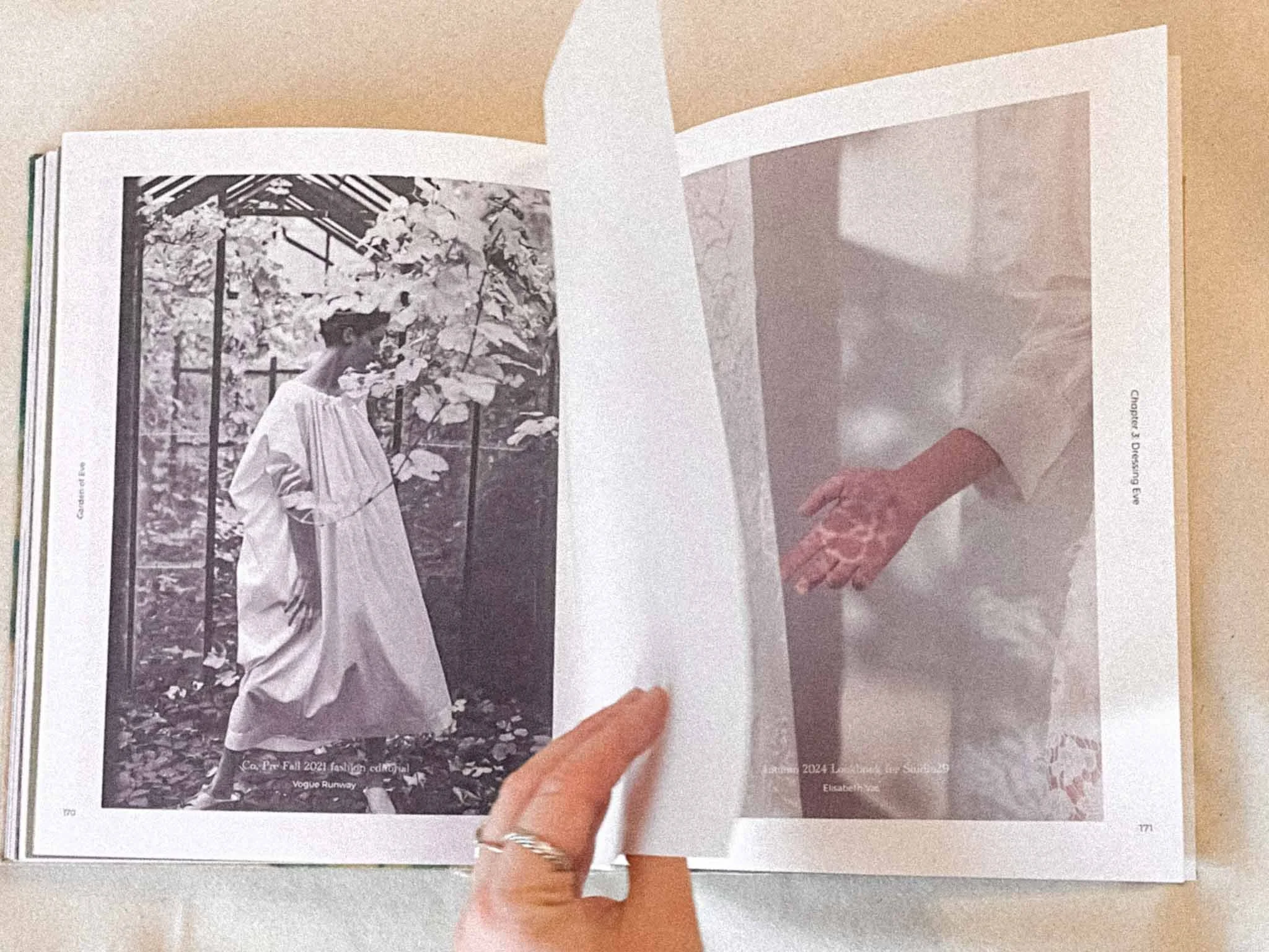 Open magazine showing a black and white fashion photograph of a woman in a long dress with leaves on the ground and a fence behind her.