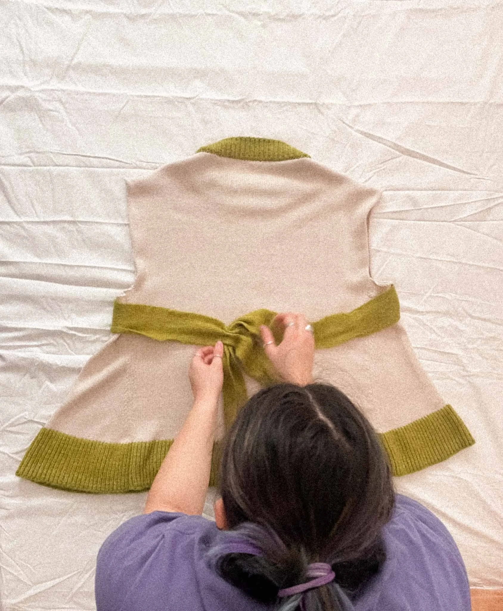 A woman photographed from above, arranging a knitwear piece as a flat lay.