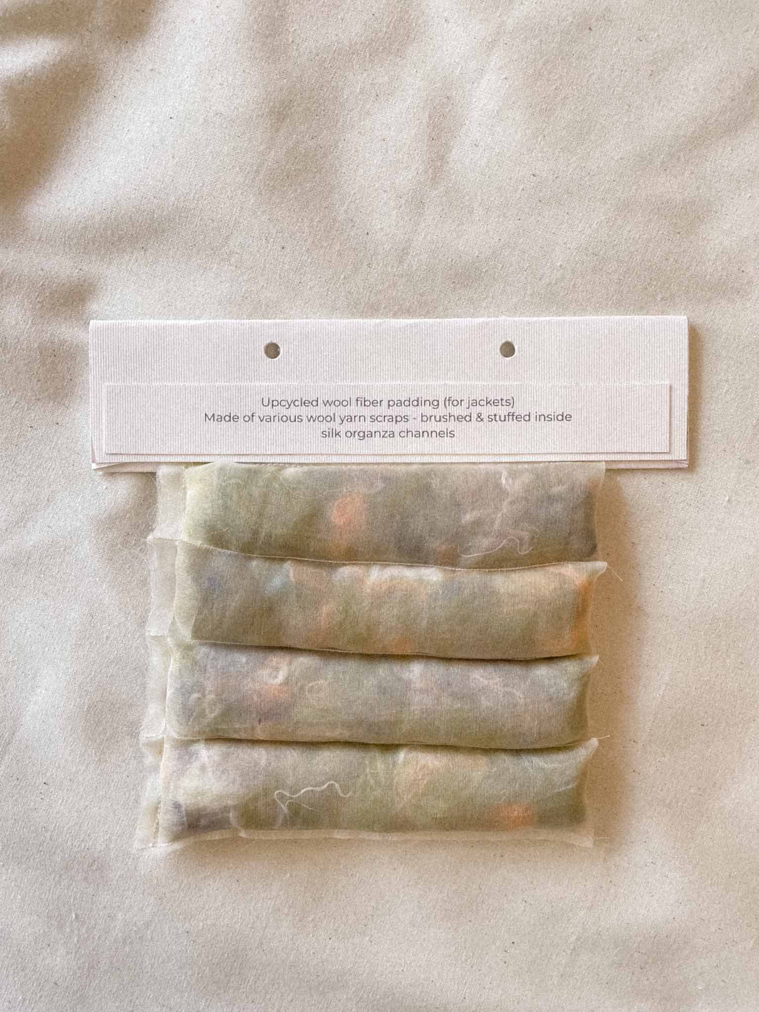 A package of upcycled wool fiber padding for jackets, made of various wool yarn scraps brushed and stuffed inside silk organza channels.