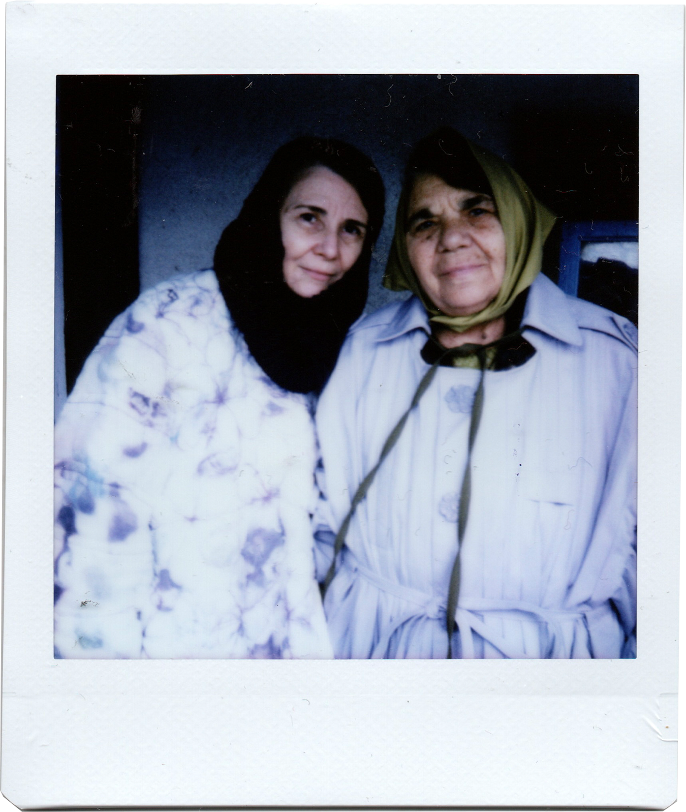 Two women wearing headscarves standing close together in front of a dark background.