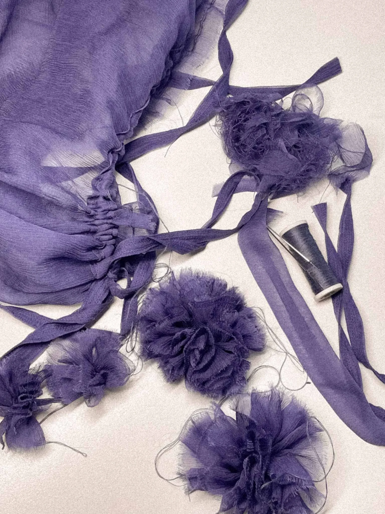 A bundle of purple fabric, ribbons, and tulle on a white surface, with a spool of purple thread nearby.