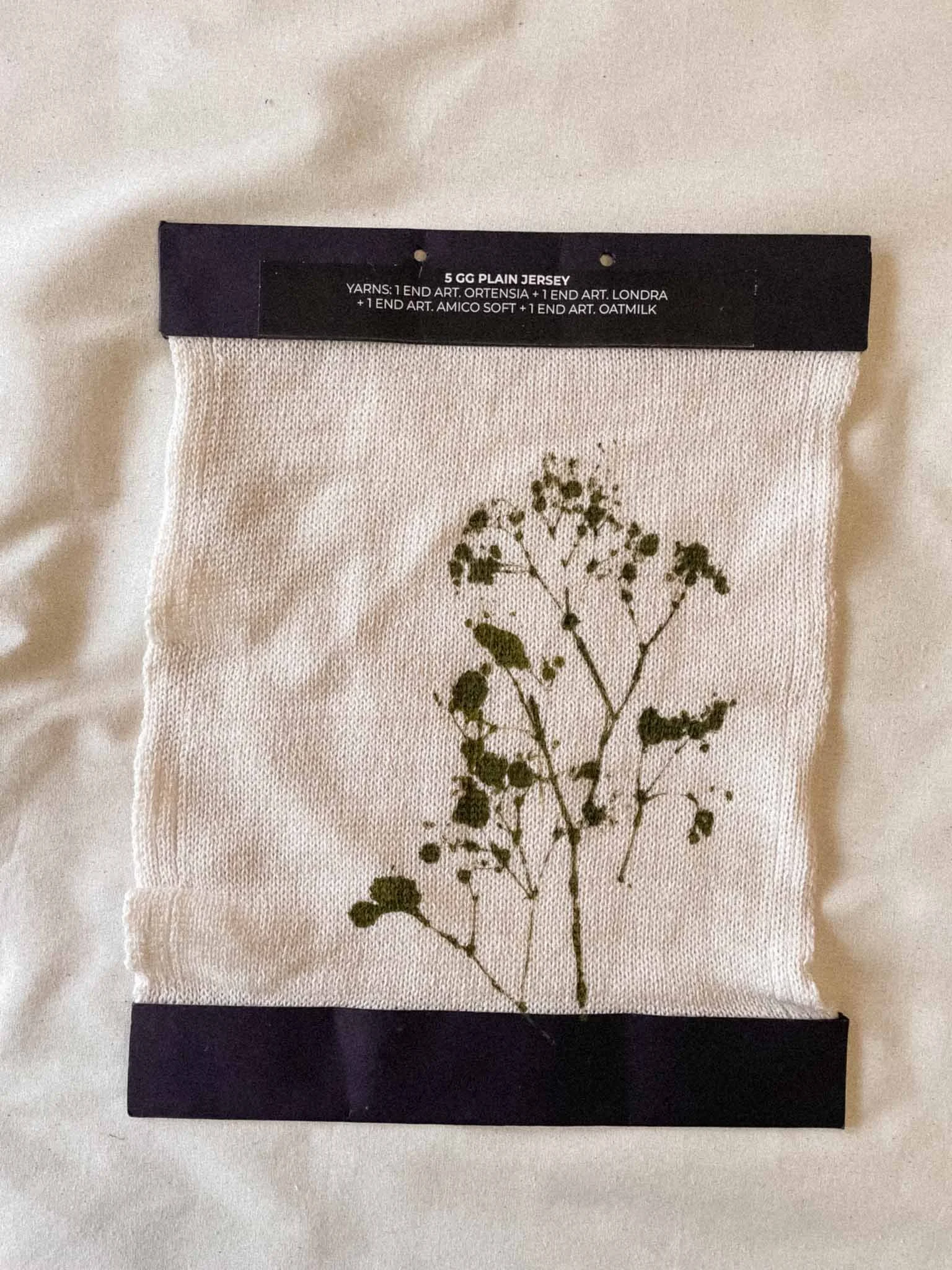 A white fabric pouch with a black border at the top and bottom, featuring a printed botanical illustration of a plant with small leaves and flowers.