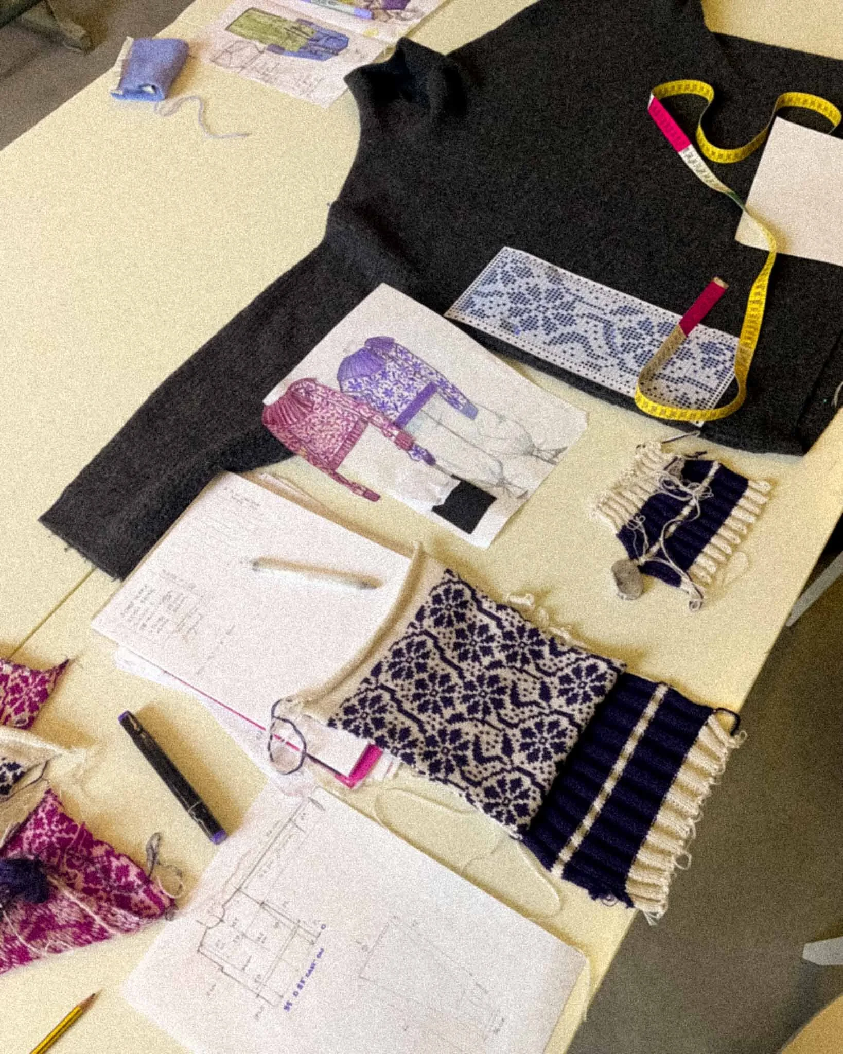 Work table with sewing samples, a measuring tape, drawings, fabric swatches, and a knitting project.