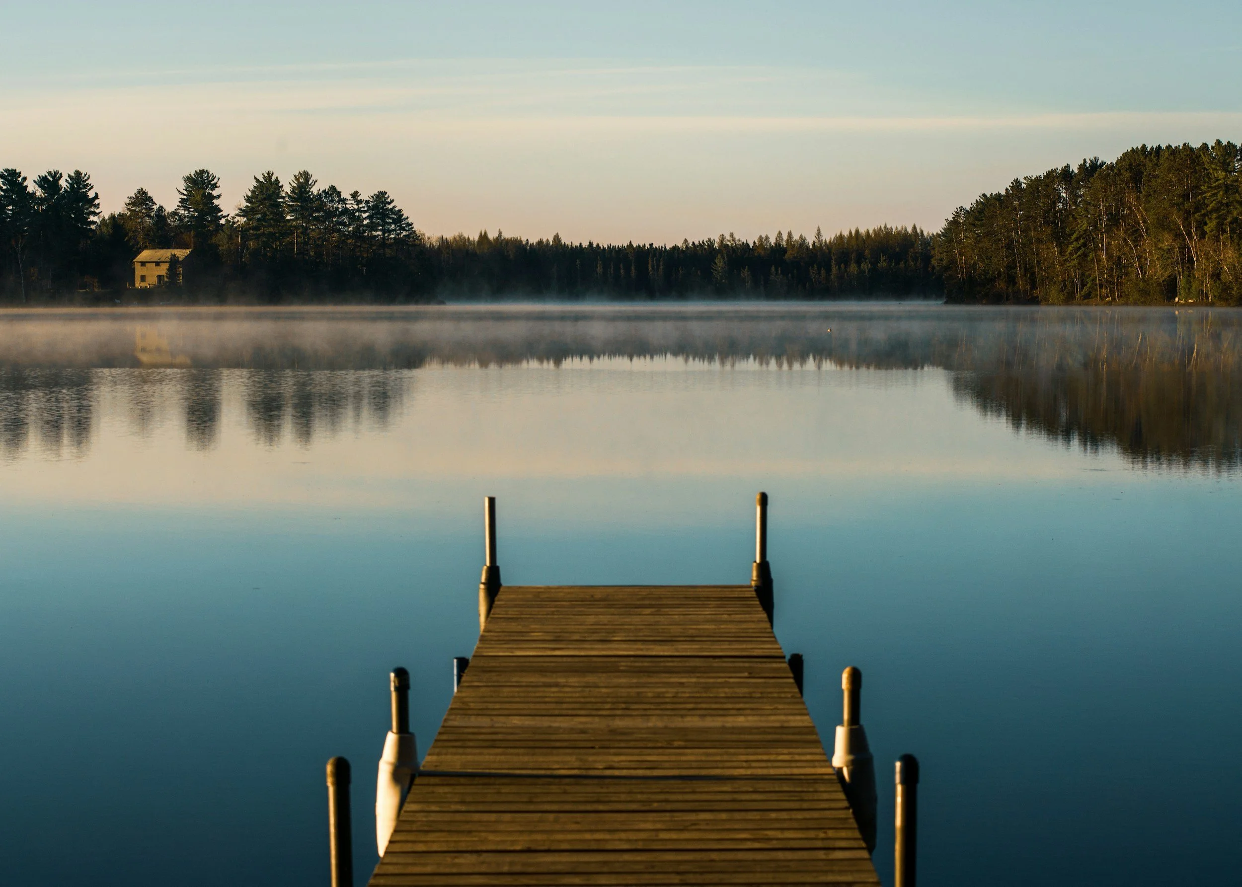A wooden dock stretching out onto the water of a lake with forest on the far shore.