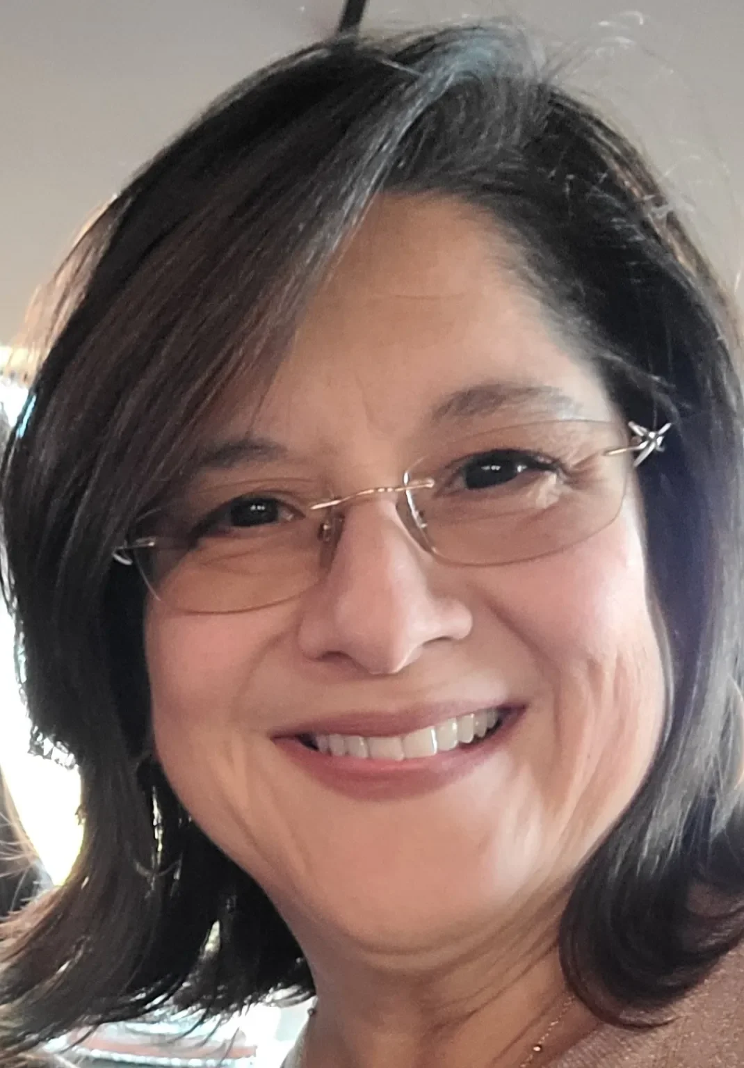 Close-up of a smiling woman with shoulder-length dark hair, wearing glasses and a necklace.