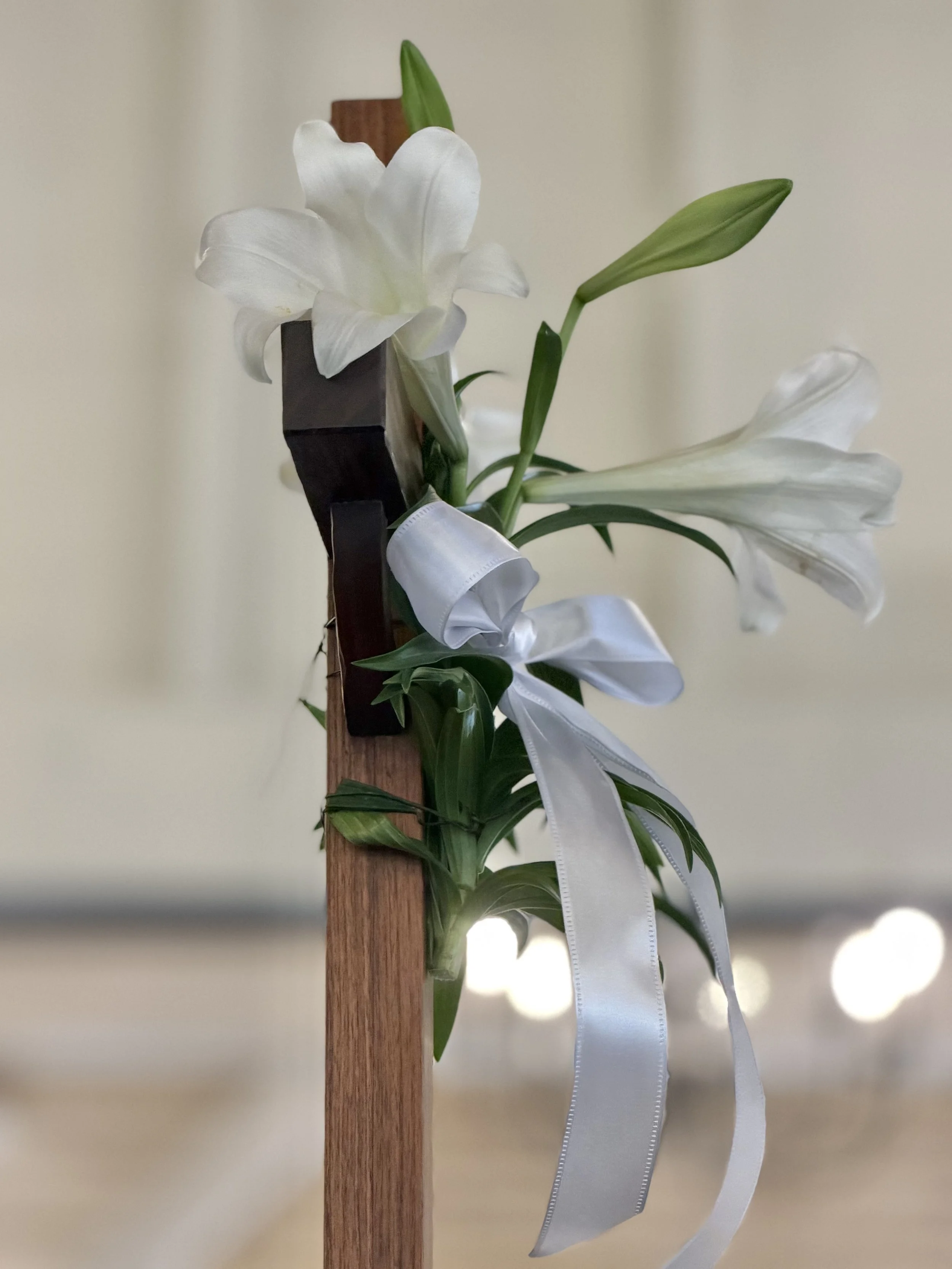 White lilies with green leaves attached to a wooden post, decorated with a white ribbon.