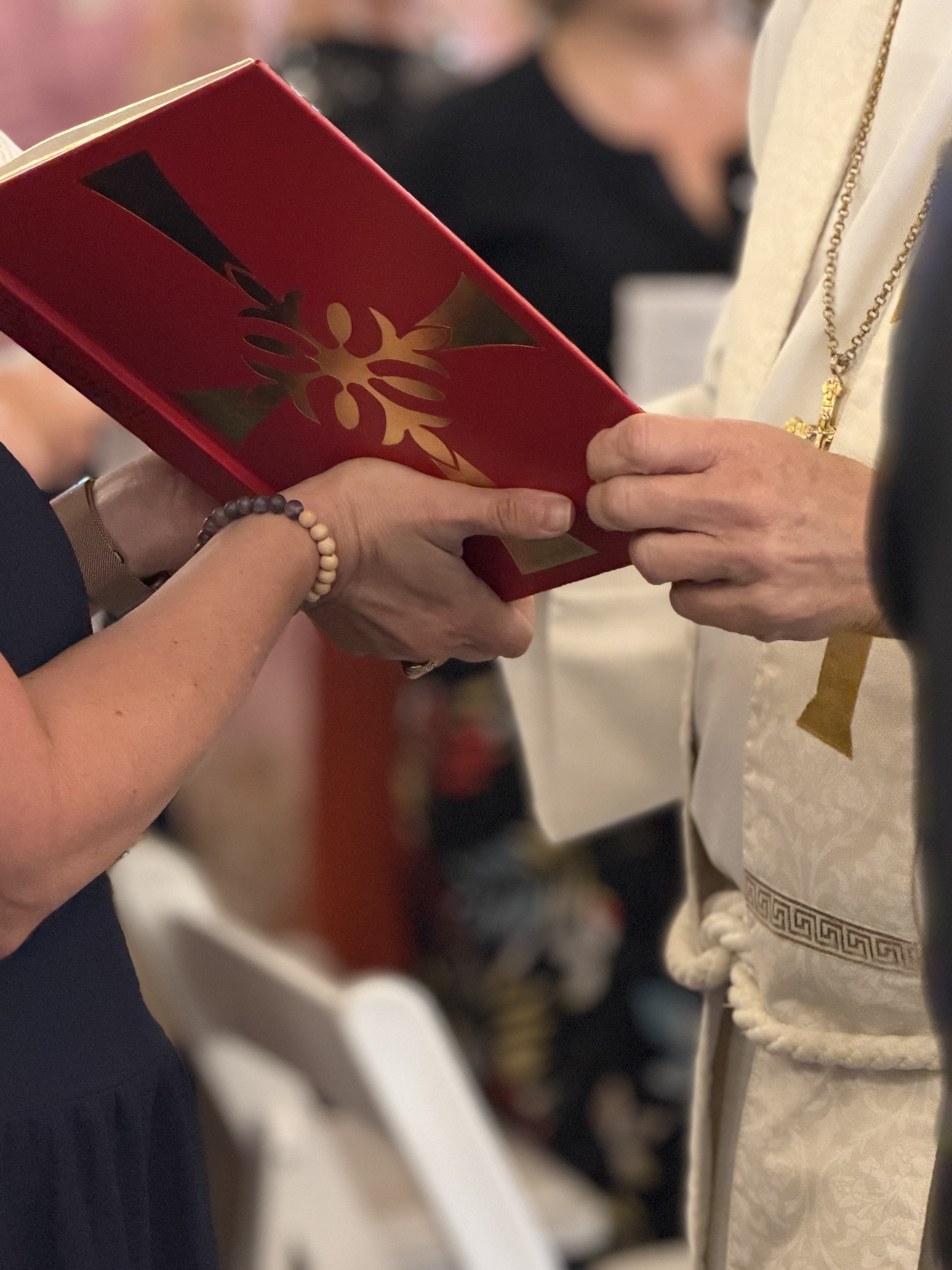 Close-up of a person in religious attire shaking hands with another individual holding a red and gold book or folder.