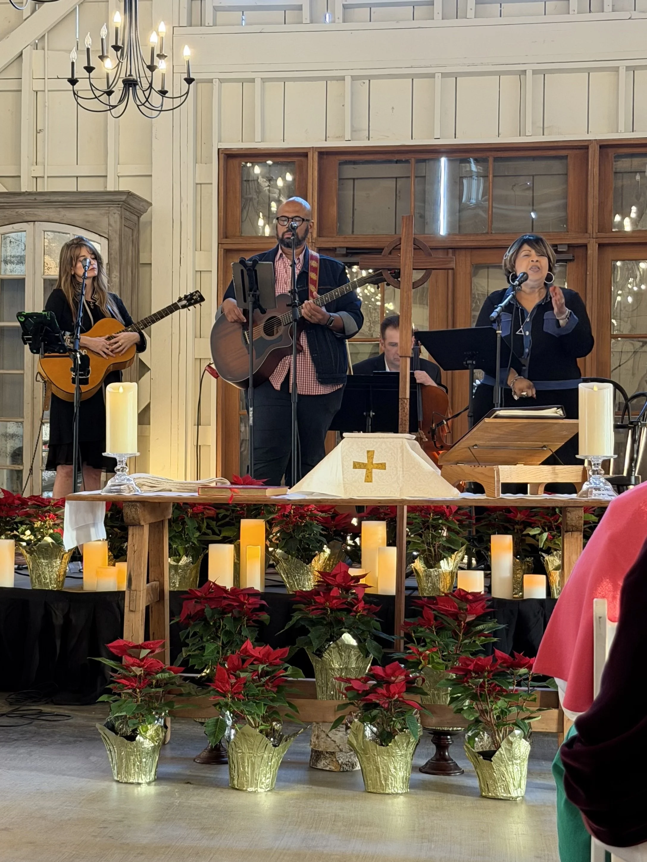 Church altar decorated with red poinsettias and candles, with a musical group performing in front of a wooden backdrop, during a Christmas service.