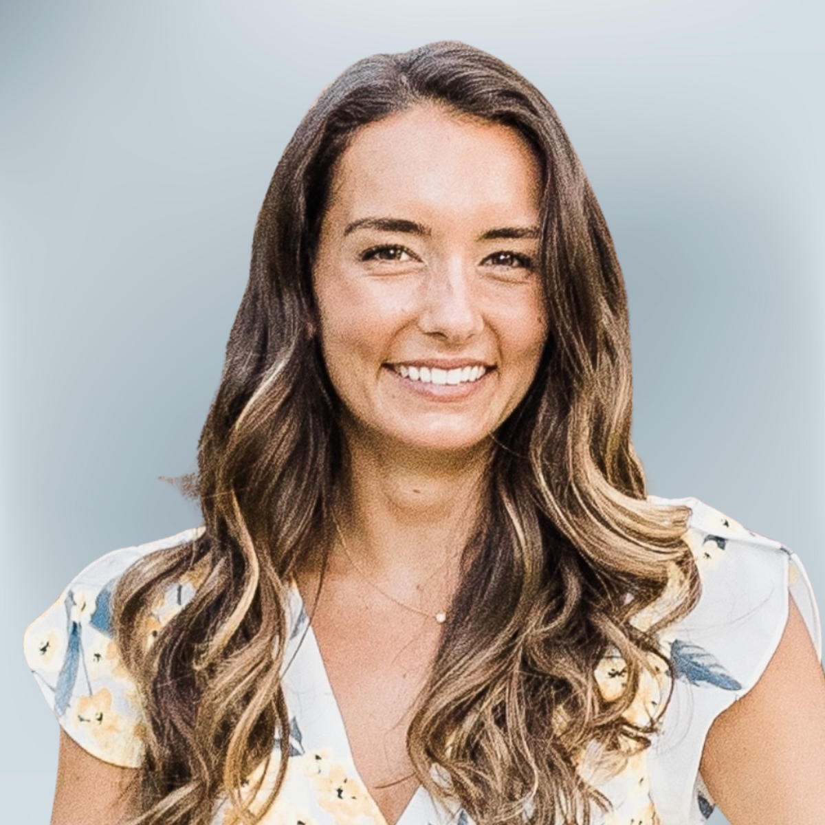A smiling woman with long wavy brown hair wearing a light-colored floral dress against a light blue gradient background.