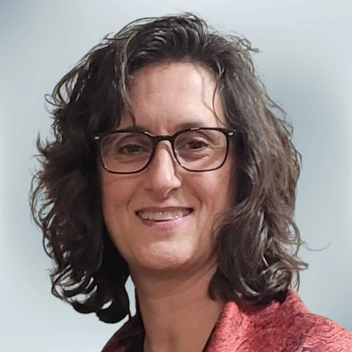 A woman with curly dark hair and glasses, smiling against a plain background.
