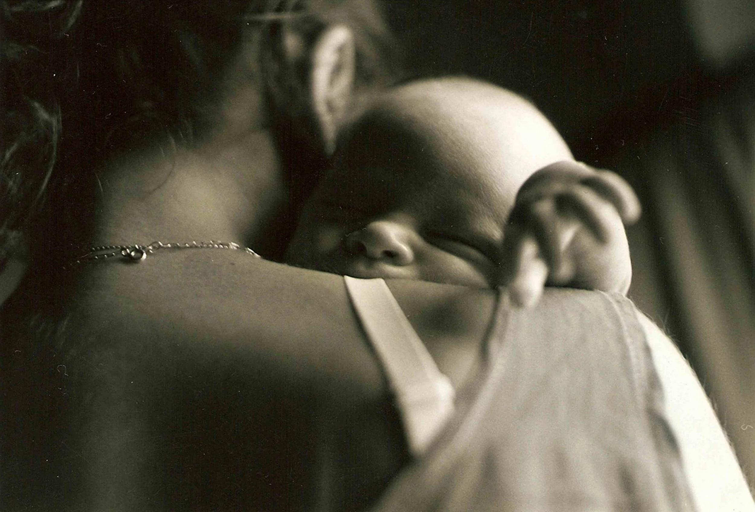 A young girl is sleeping while resting her head on an adult's shoulder. The scene is intimate and peaceful, captured in black and white.