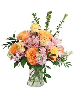 A bouquet of pink and yellow roses with other pink flowers and green foliage in a clear glass vase.