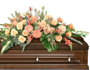 Flower arrangement on top of a closed wooden casket, including various pastel-colored flowers and green leaves.