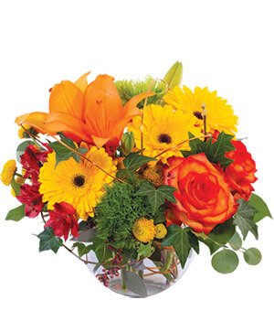A colorful flower arrangement in a glass vase featuring orange lilies, yellow daisies, red roses, and green foliage.