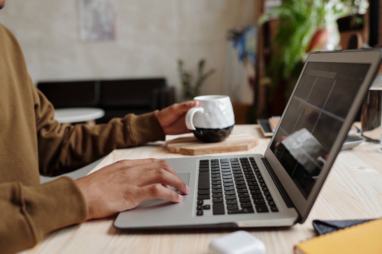 A person of colour using a laptop while holding a mug